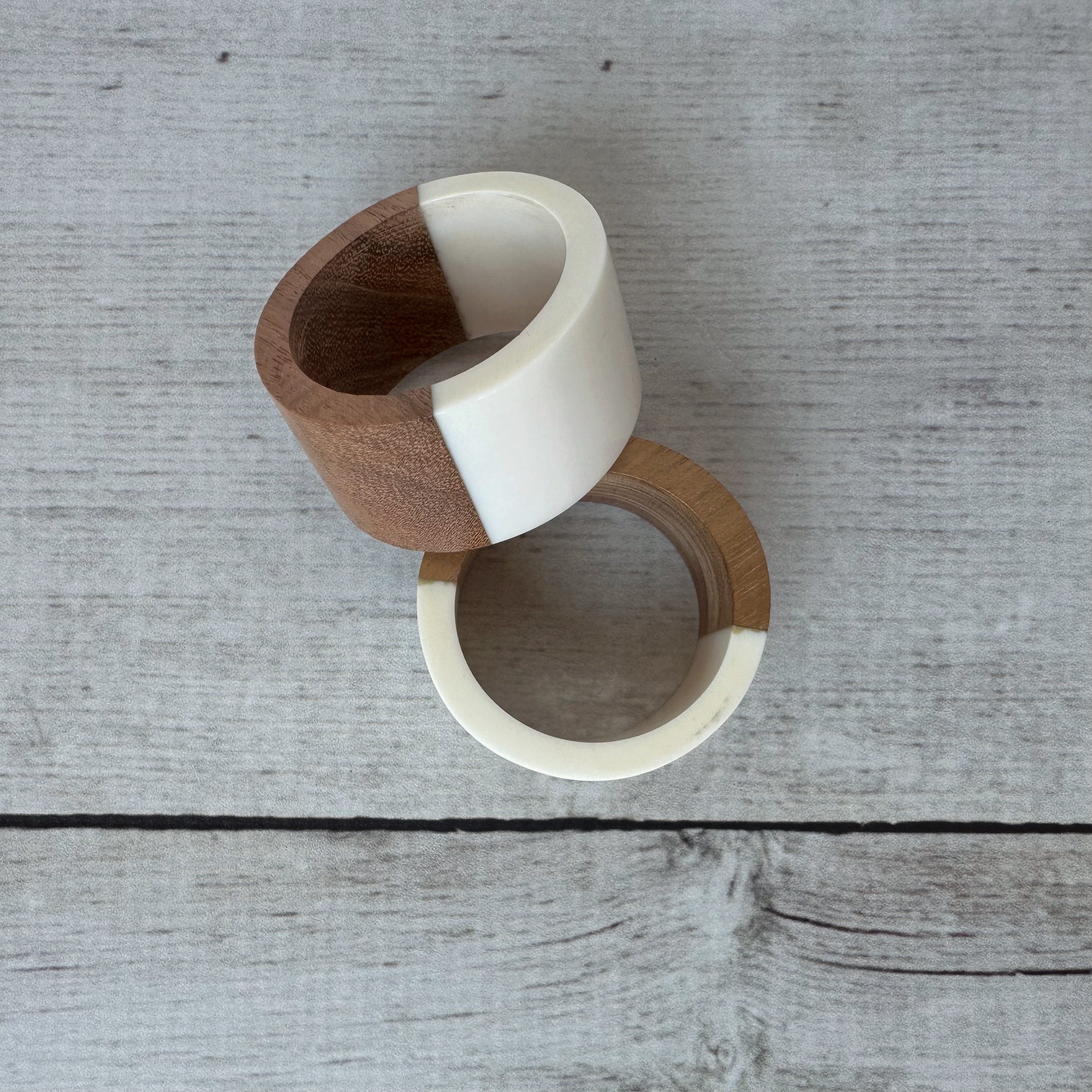 Two wooden napkin rings with white accents on a wooden surface