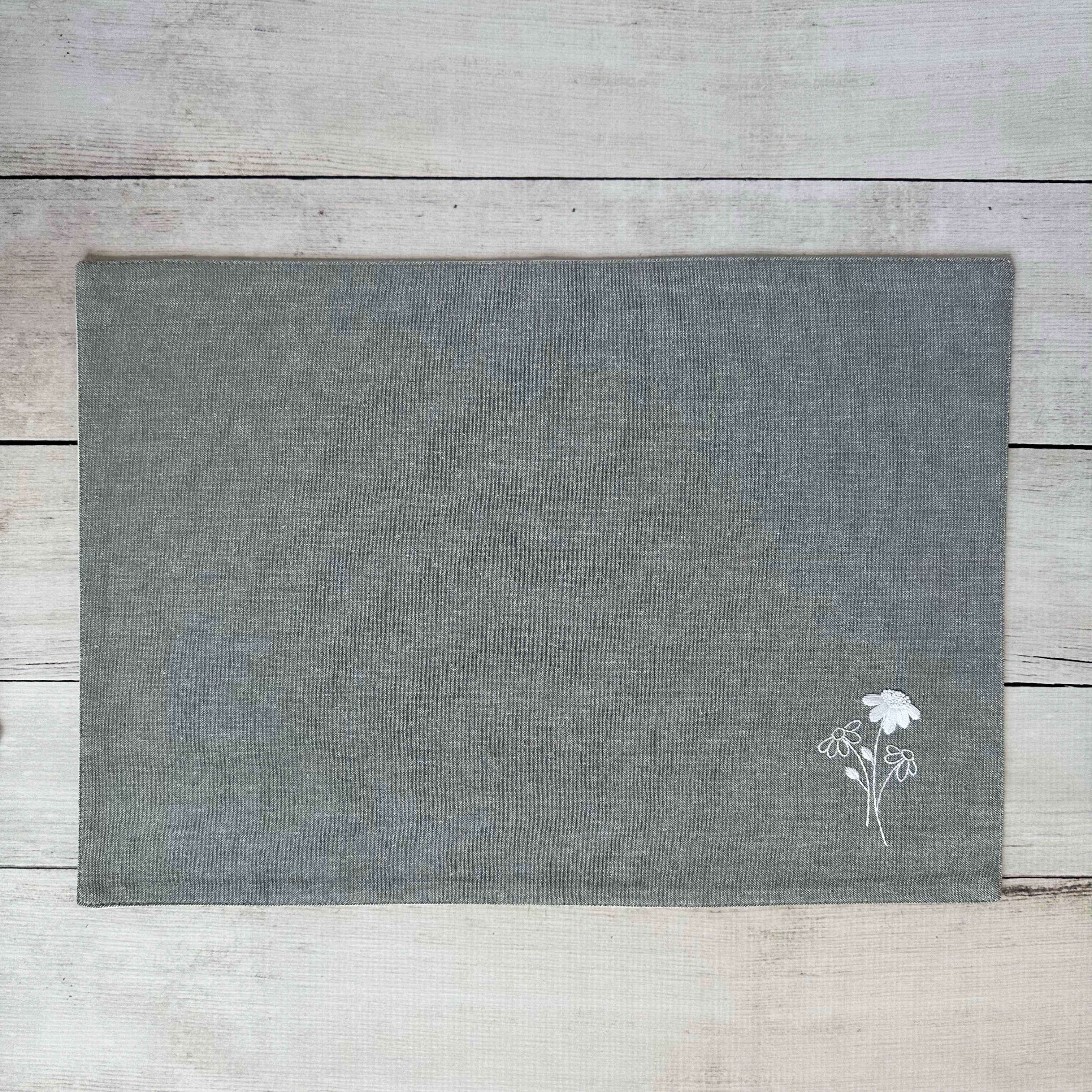 Gray cotton placemat with embroidered floral design on a wooden surface