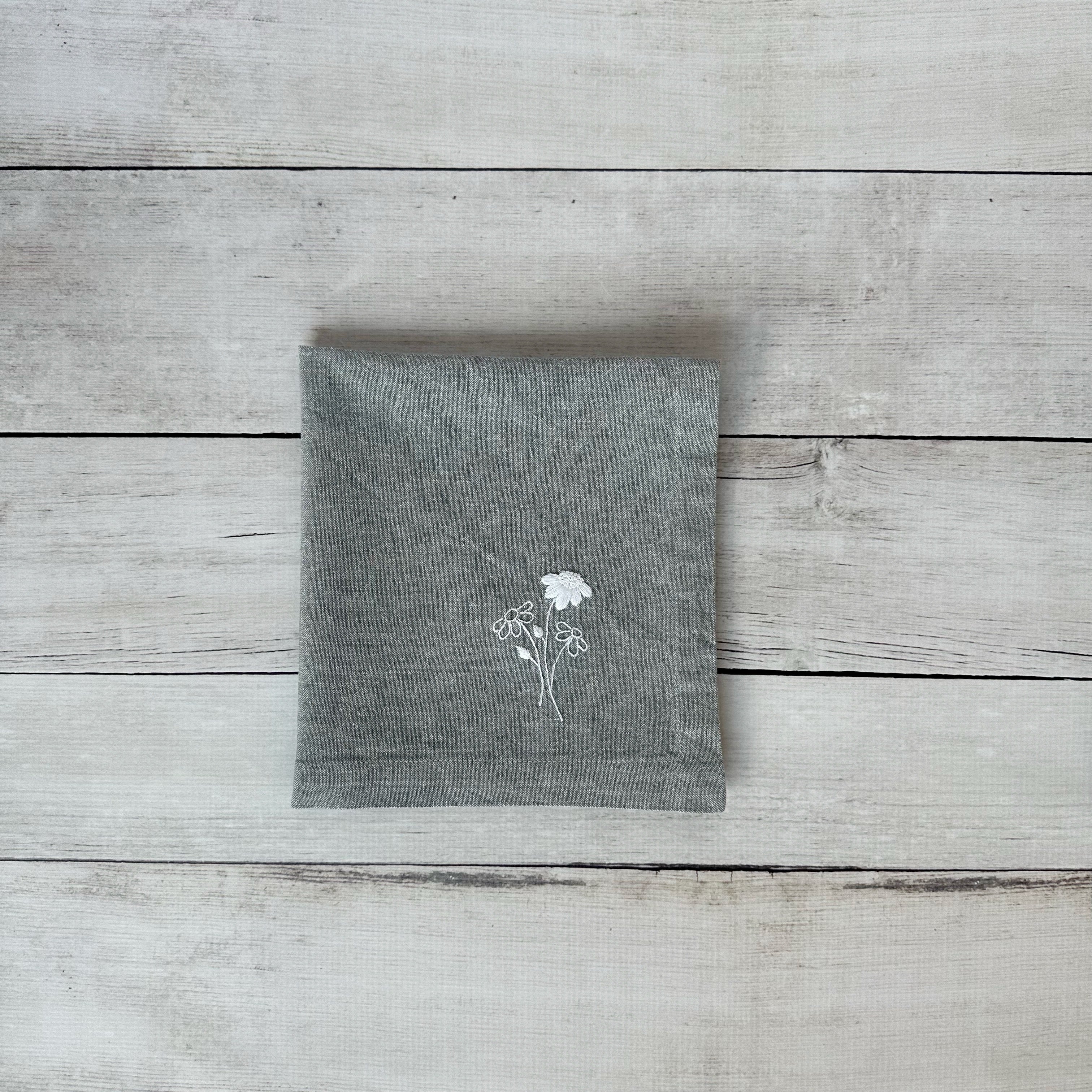Gray cotton napkin with floral embroidered design on a wooden surface