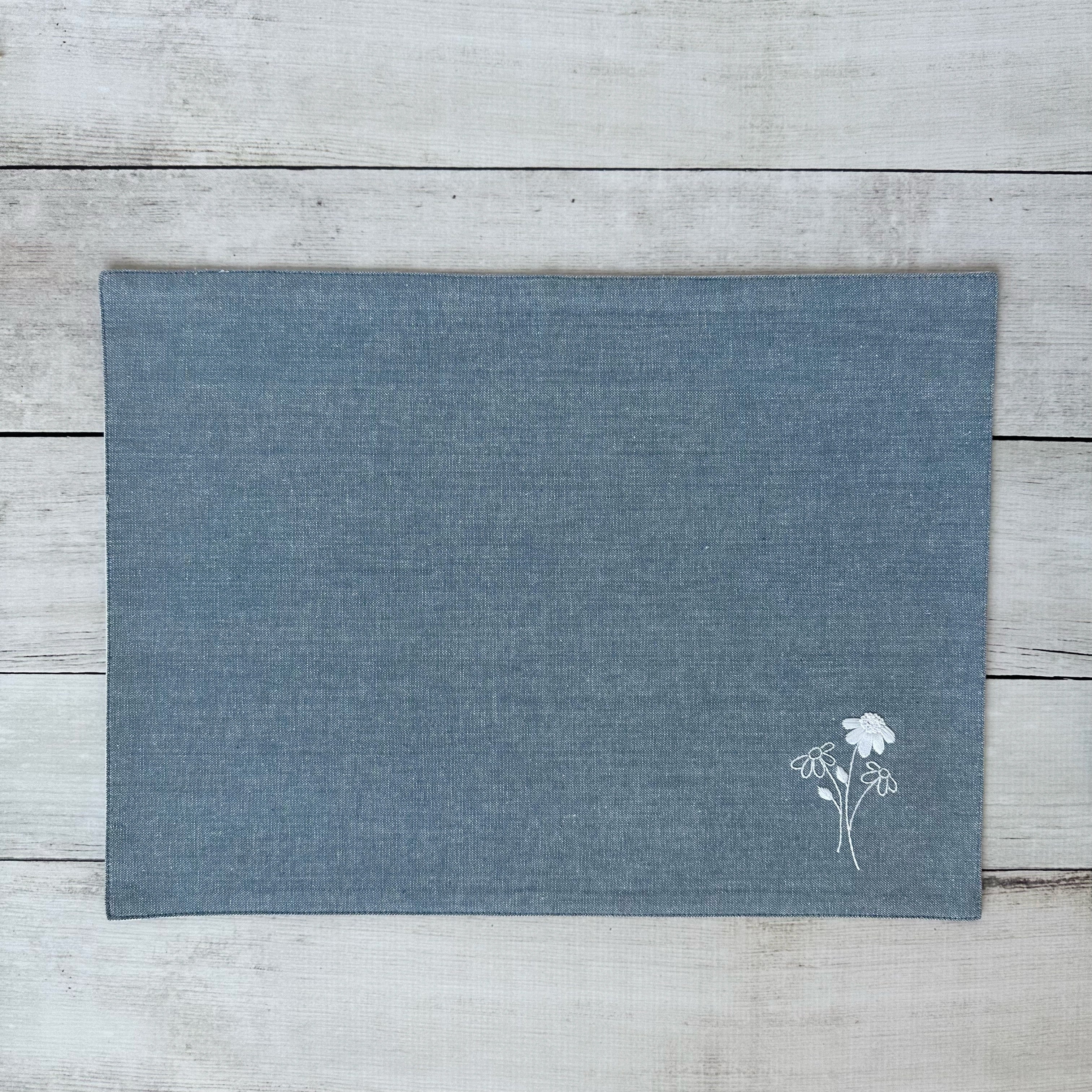 Blue cotton placemat with embroidered floral design on a wooden surface