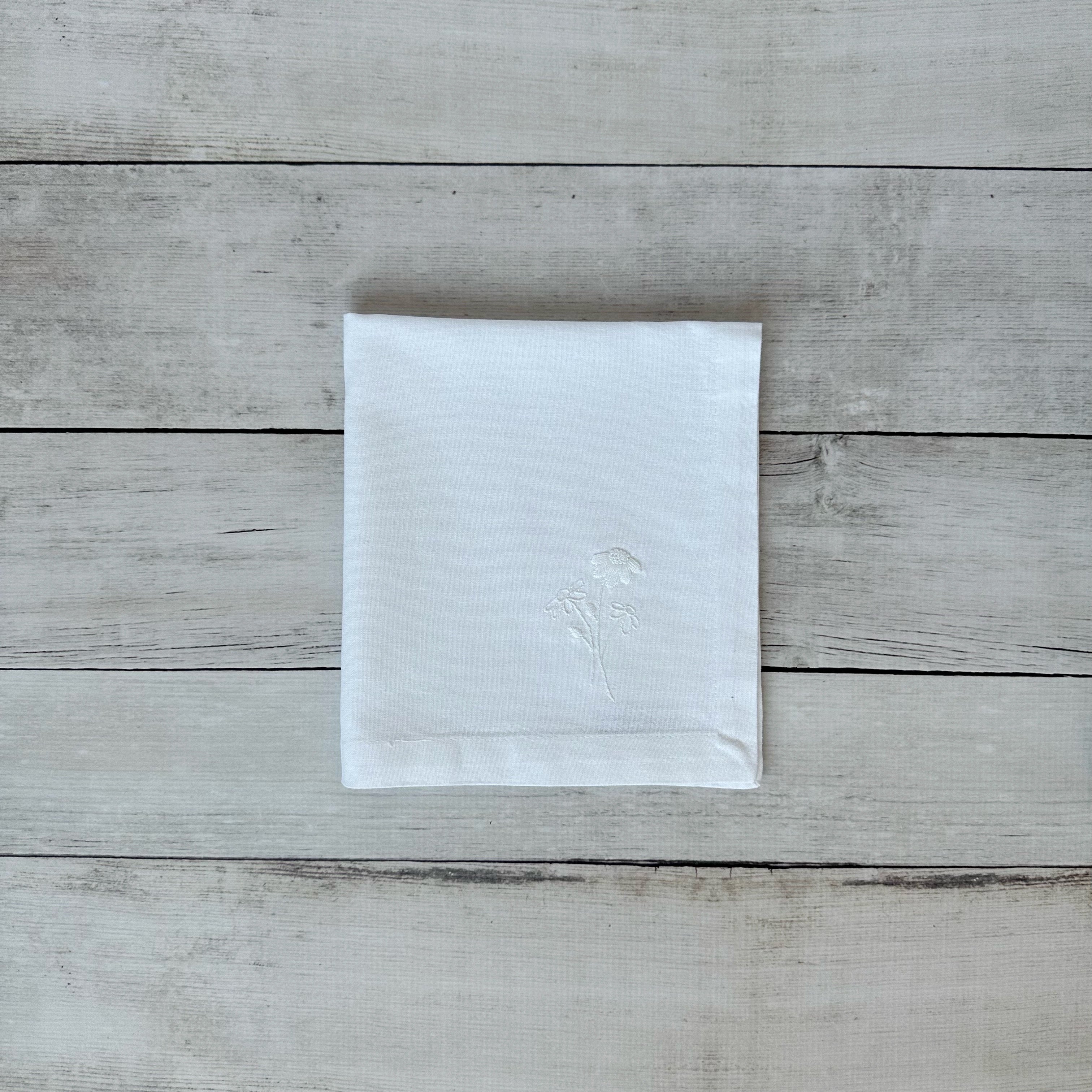 White cotton napkin with floral embroidered design on a wooden surface