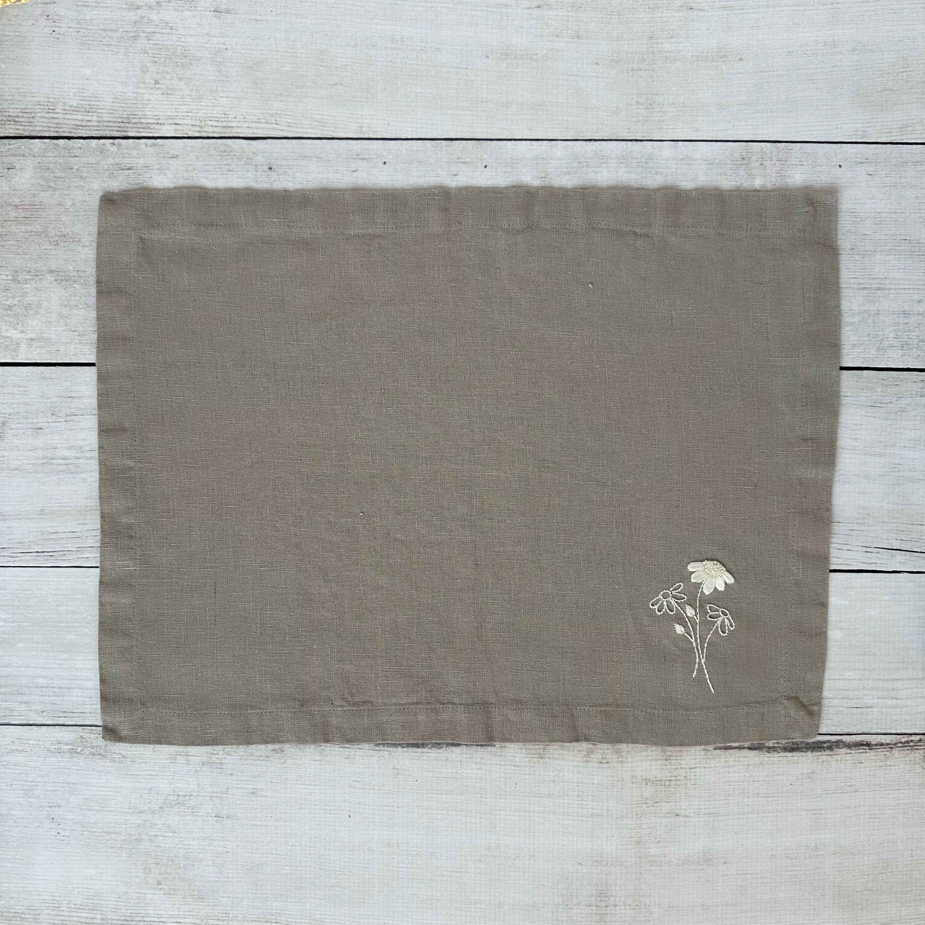 Taupe linen placemat with embroidered flowers on a wooden surface