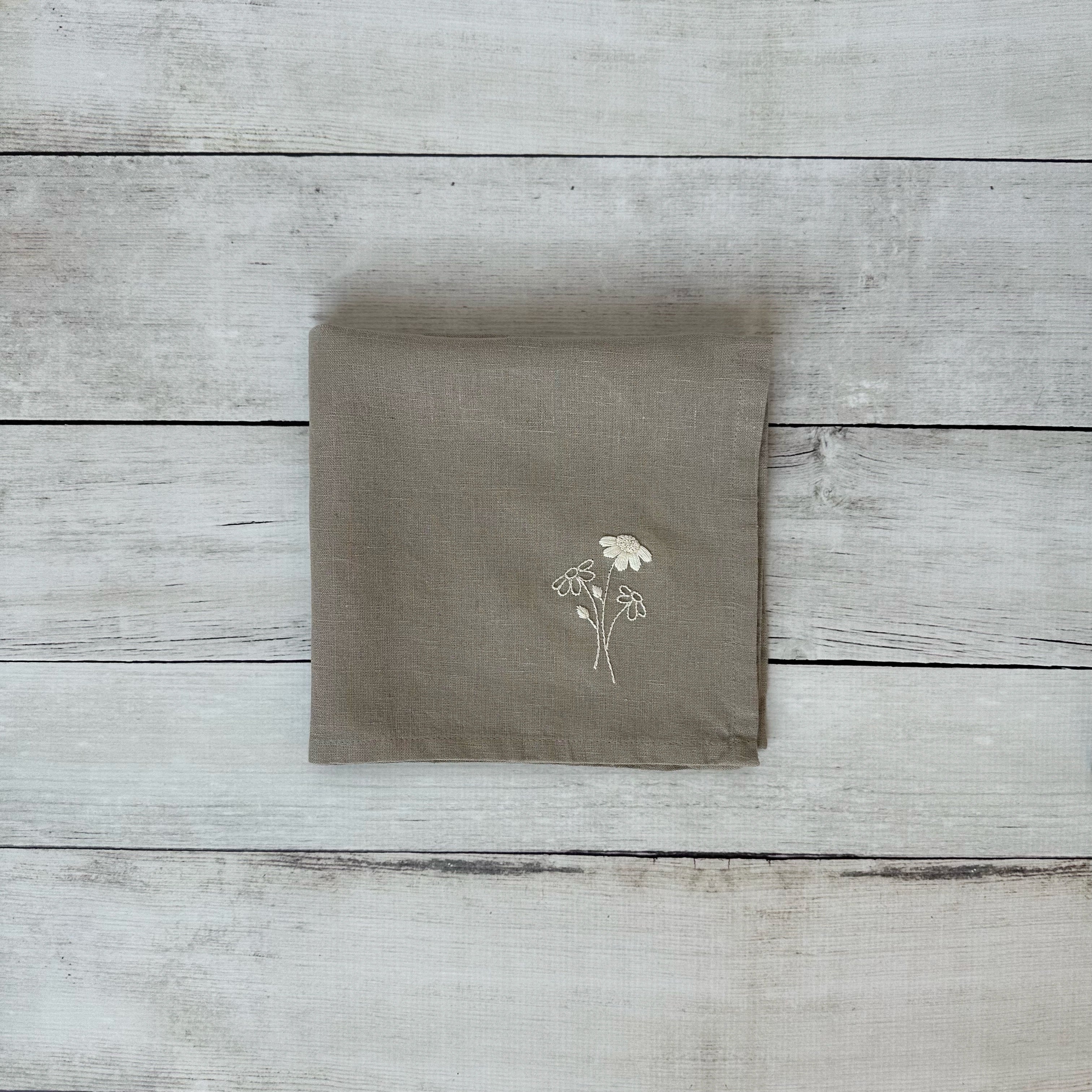 Taupe linen napkin with floral embroidered design on a wooden surface