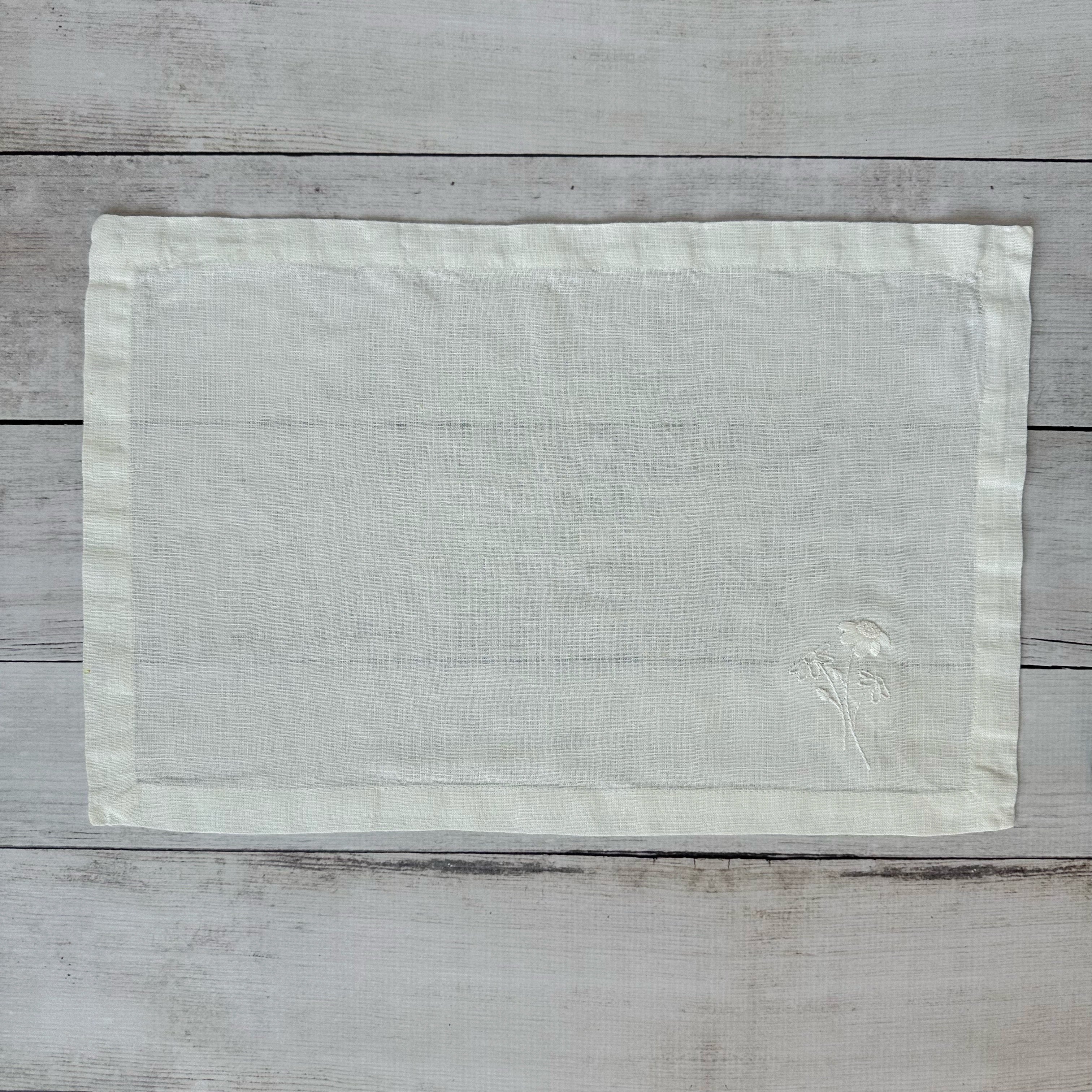 Ivory linen placemat with embroidered flowers on a wooden surface