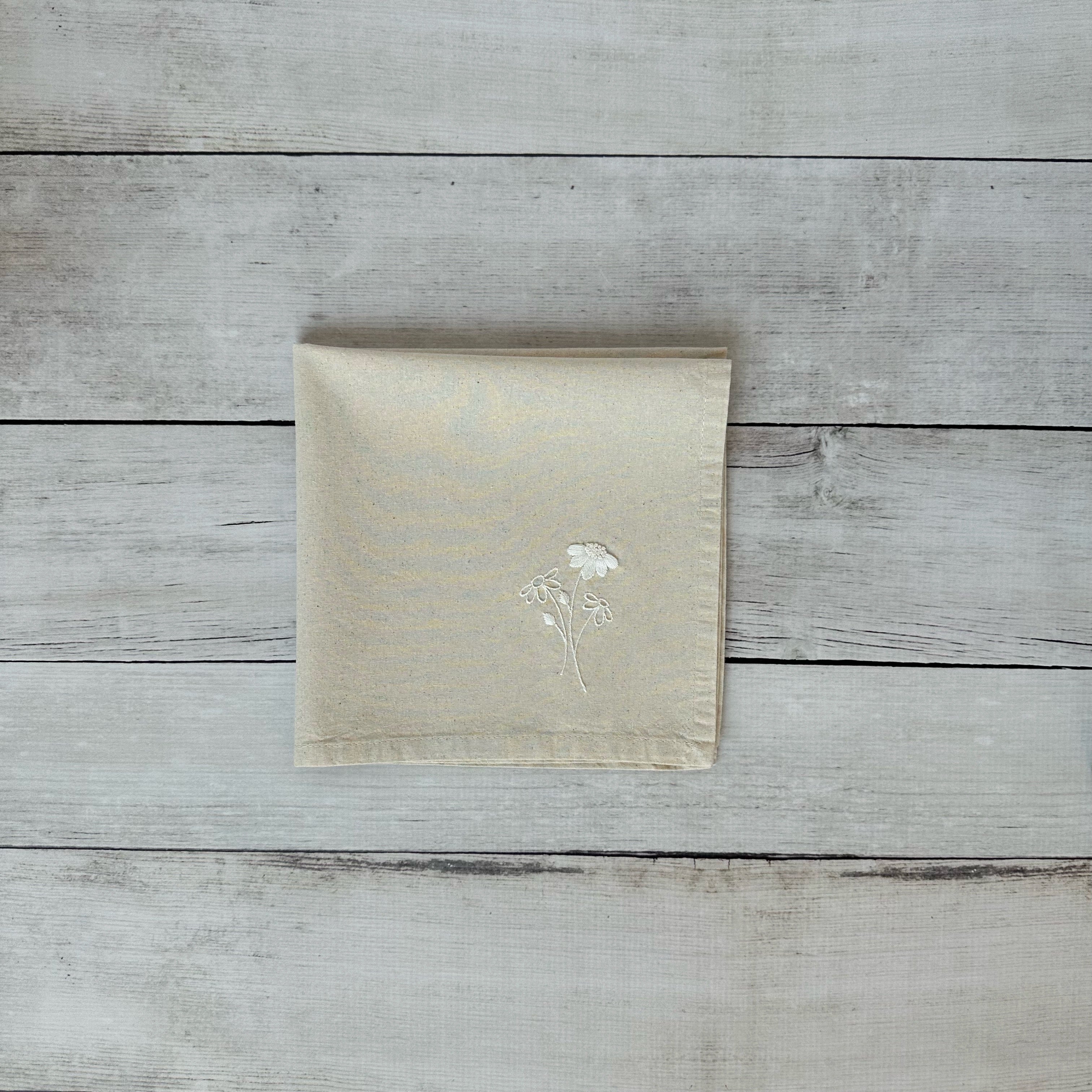 Beige napkin with embroidered floral design on a wooden surface