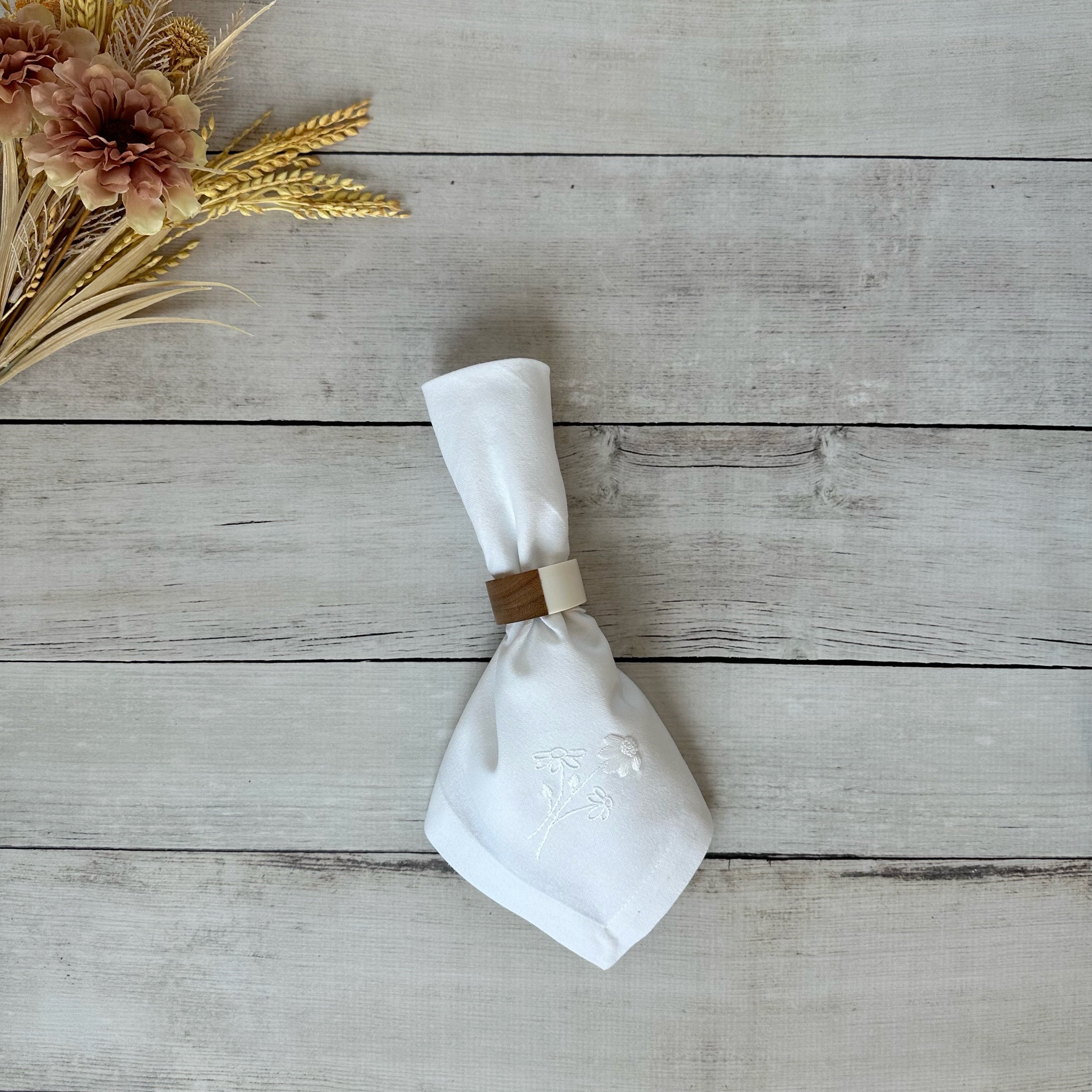 White cotton napkin with floral embroidery on a wooden surface with flowers.