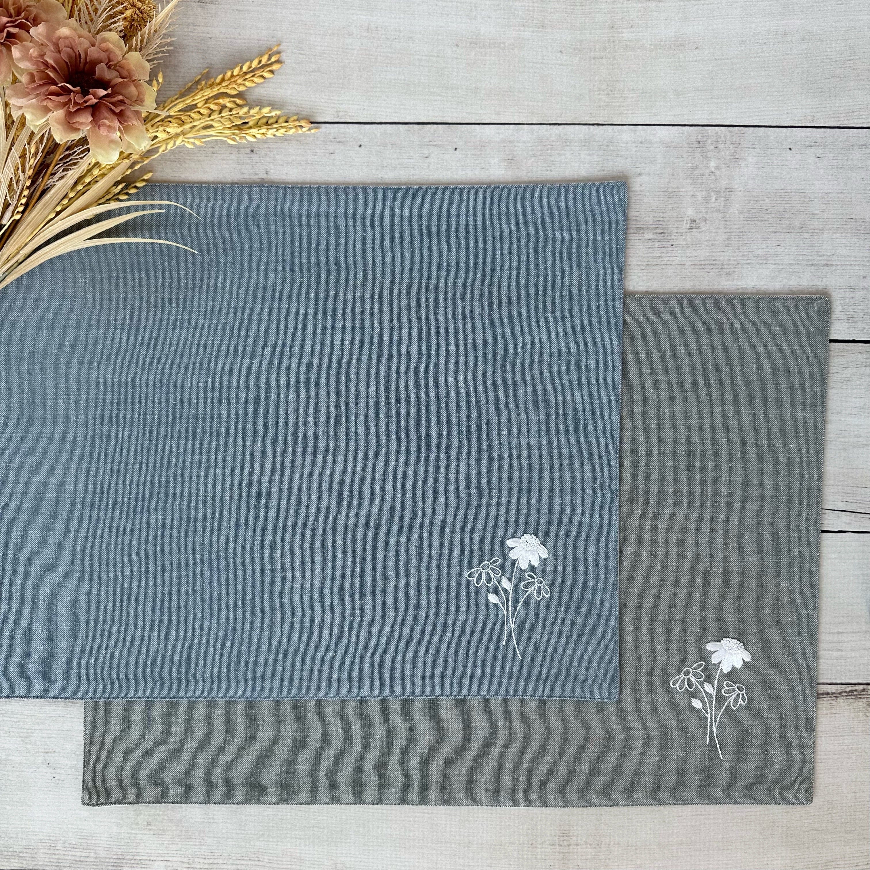 Two placemats with floral embroidery on a wooden surface.