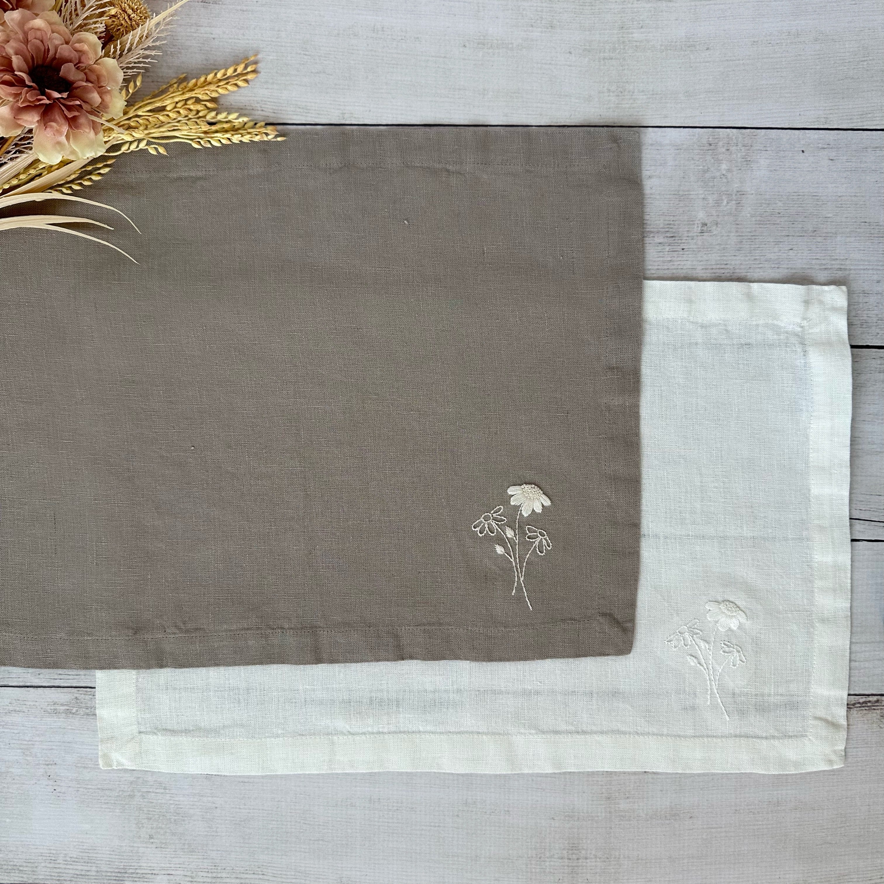 Ivory and taupe linen placemats with embroidered flowers on a wooden surface