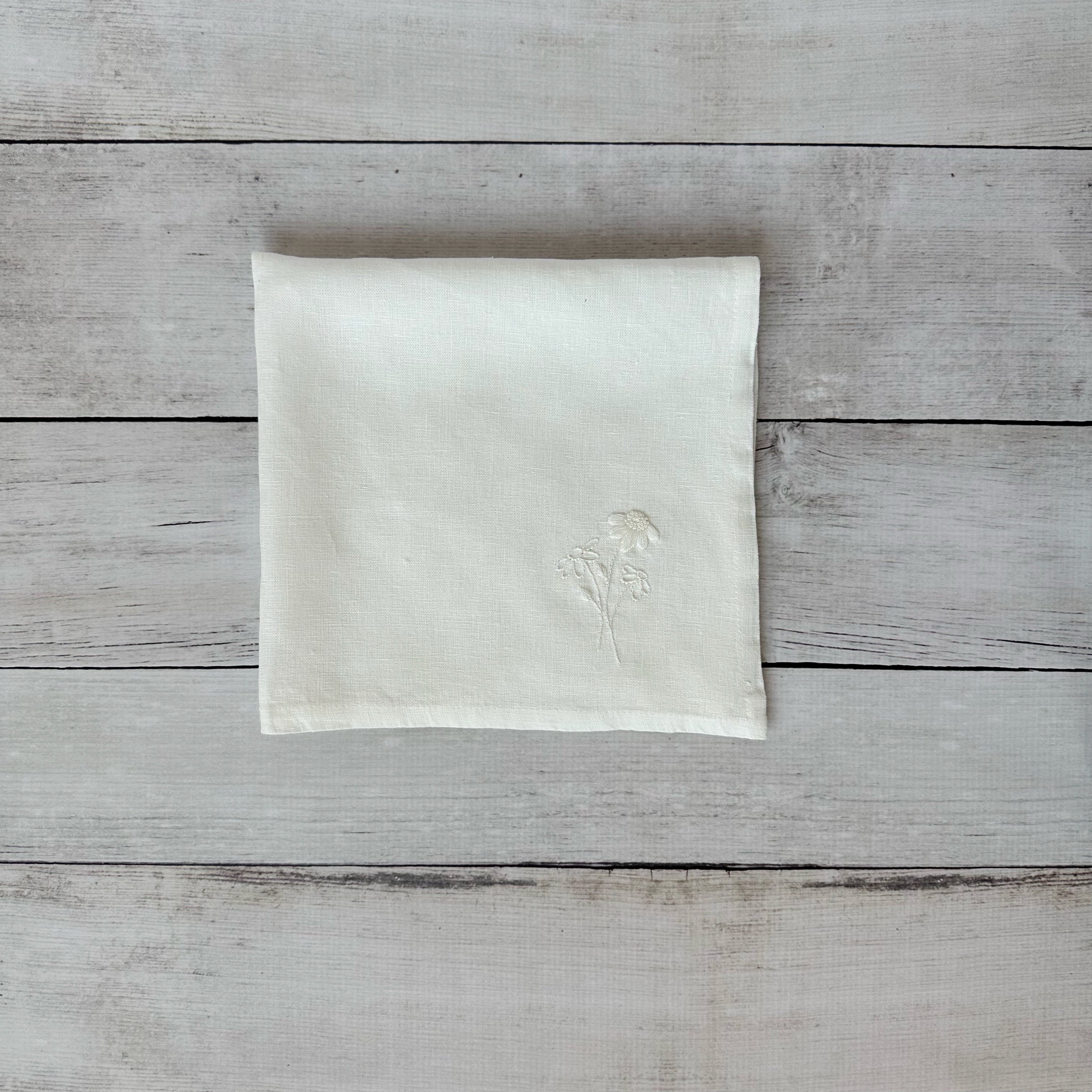 Ivory linen napkin with floral embroidered design on a wooden surface