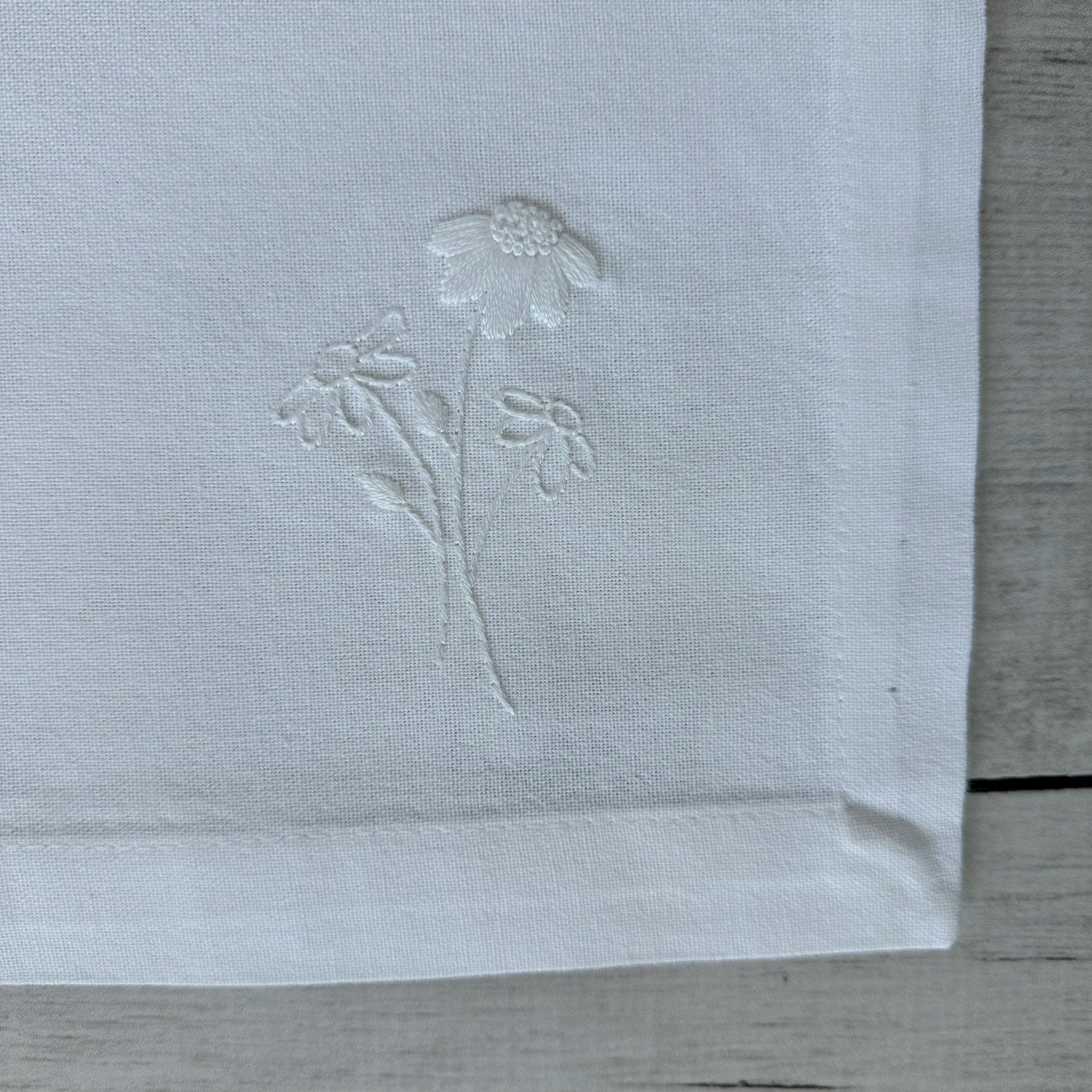 Floral embroidered design on corner of a white cotton napkin