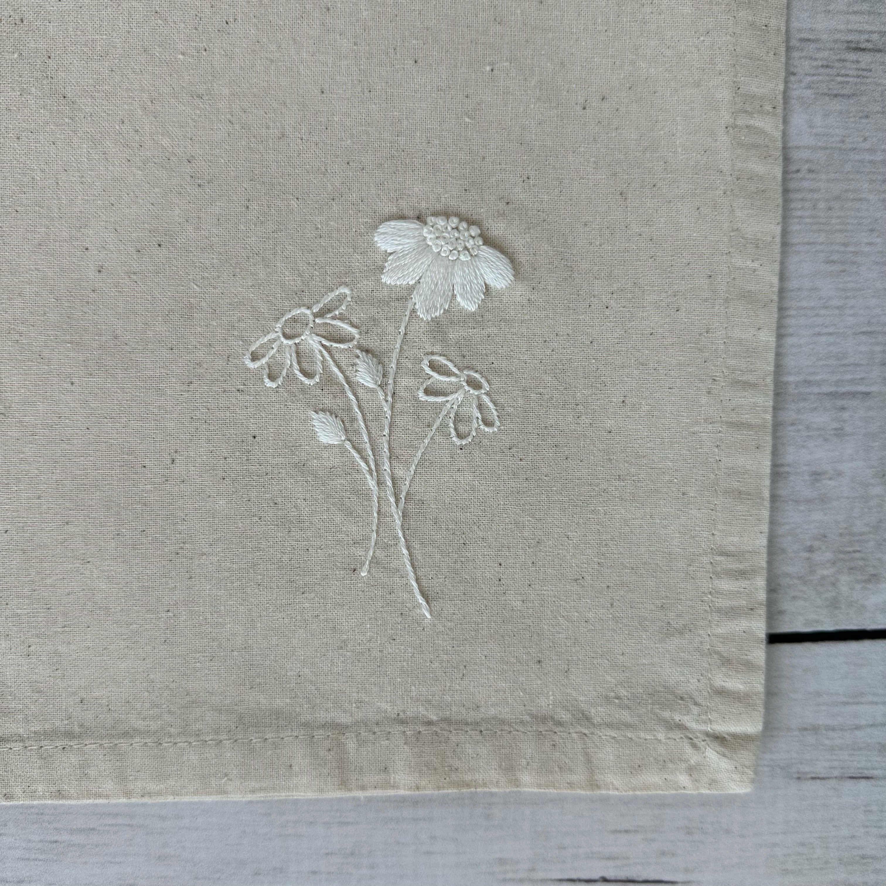 Floral embroidered design on corner of a beige cotton napkin