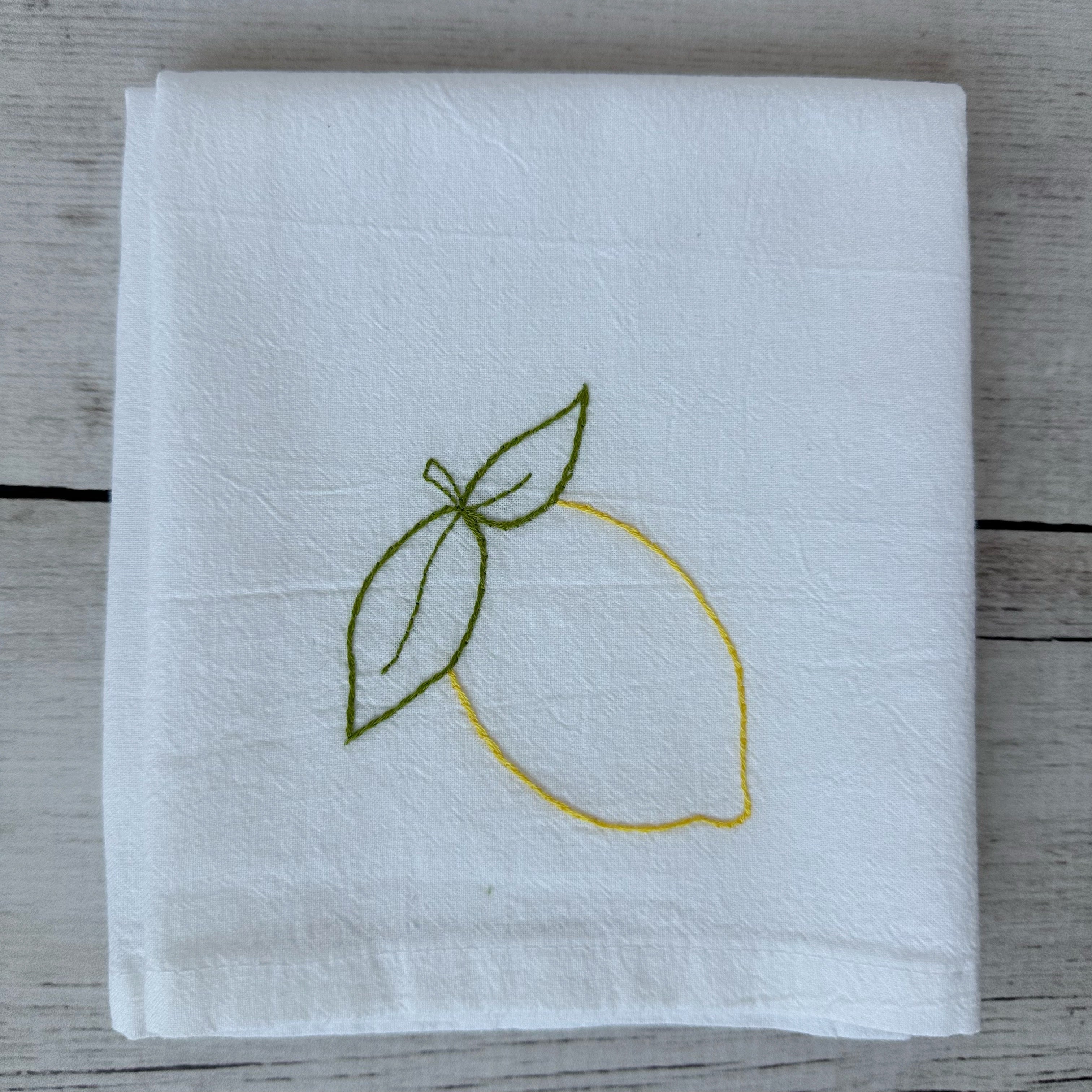 White tea towel with embroidered lemon design on a wooden surface