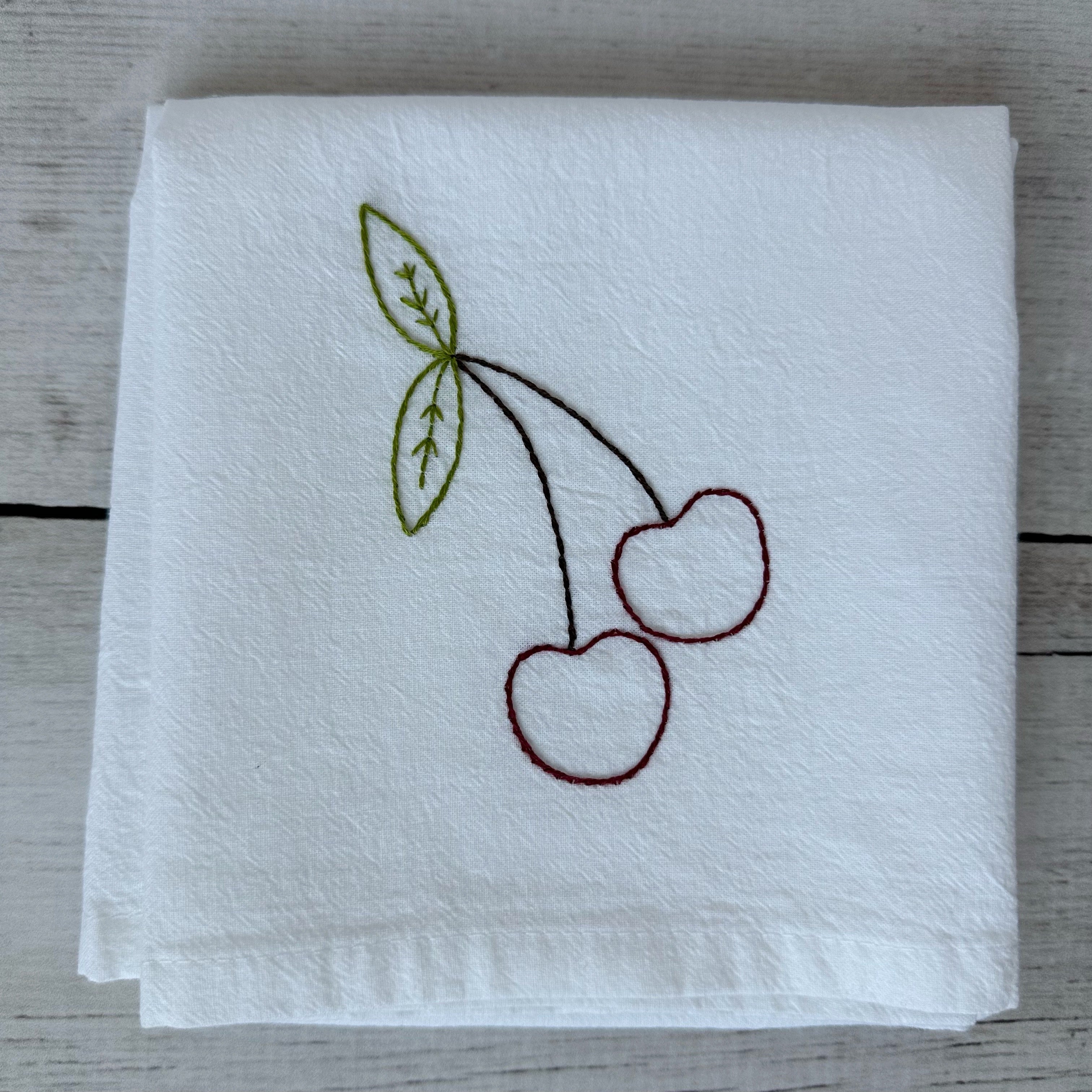 White tea towel with embroidered cherries on a wooden surface