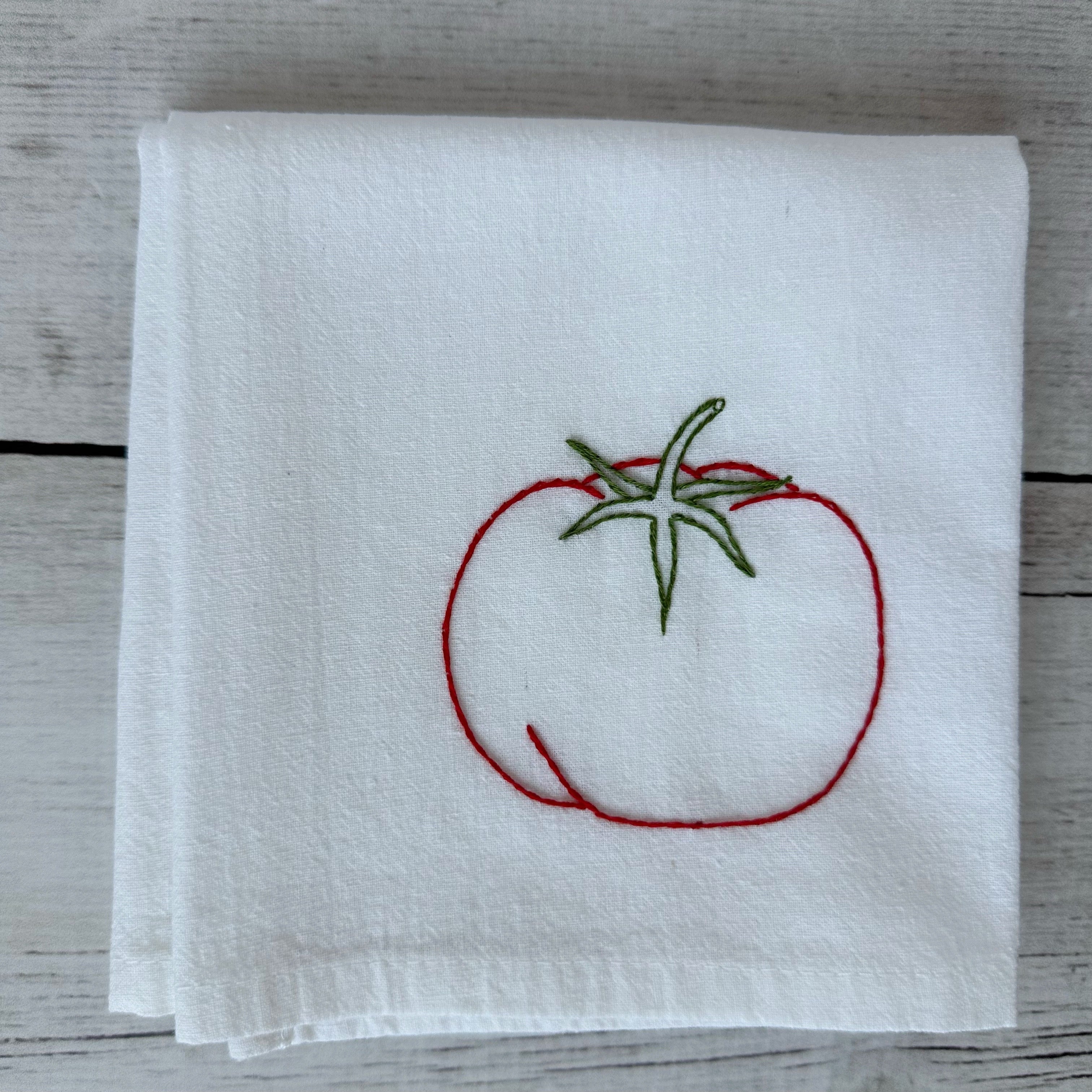 White tea towel with red embroidered tomato design on a wooden surface