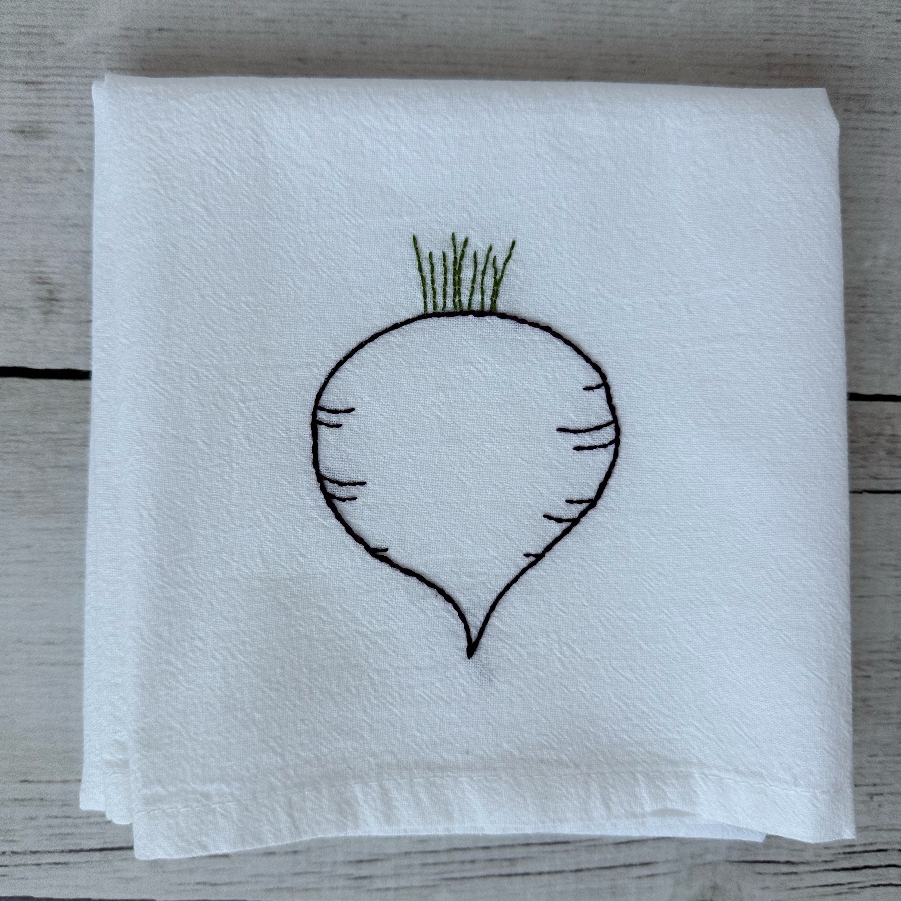 White tea towel with embroidered beet design on a wooden surface