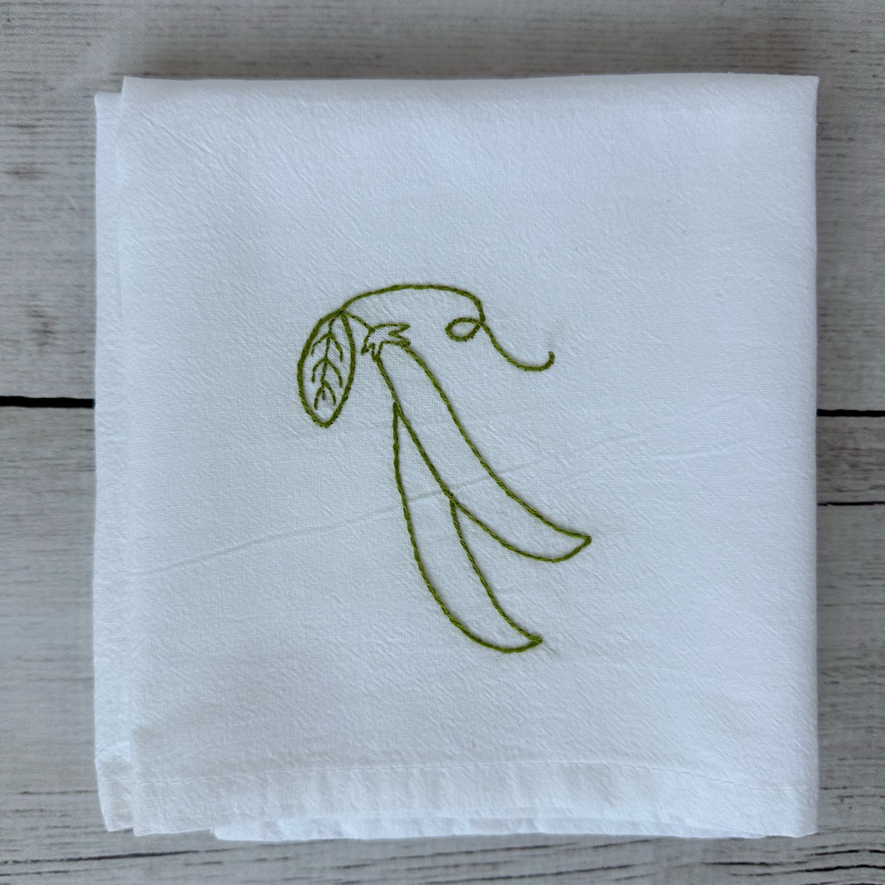 White tea towel with embroidered snap peas design on a wooden surface