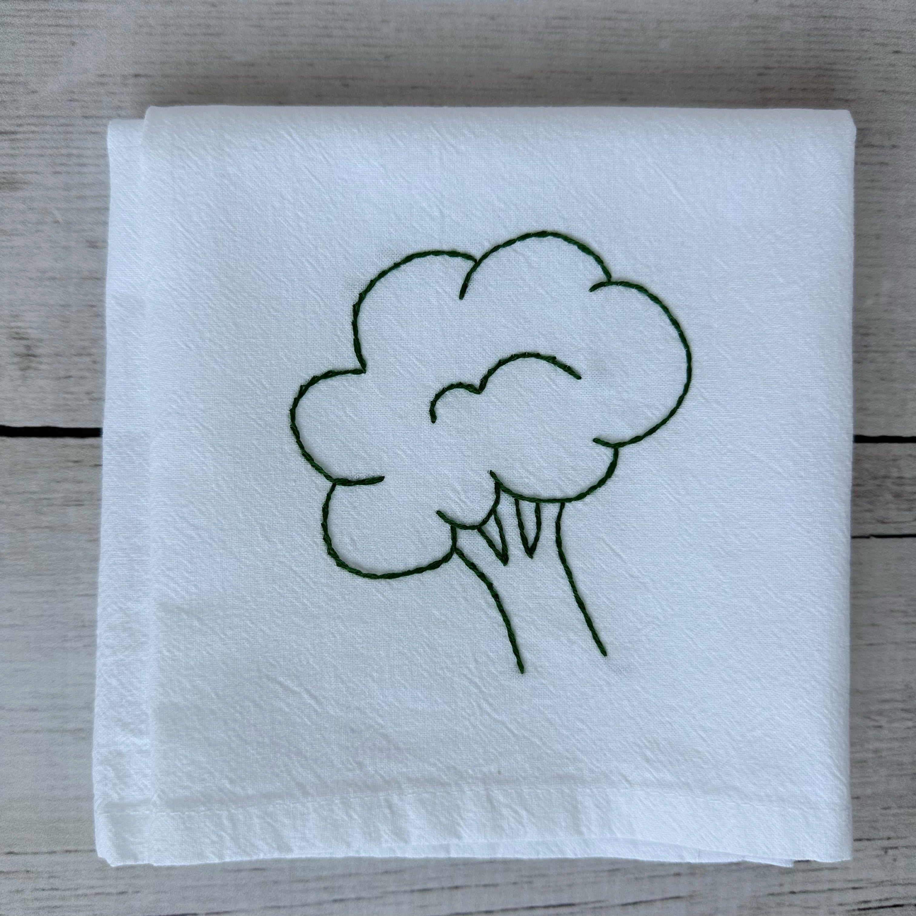 White tea towel with embroidered broccoli design on a wooden surface