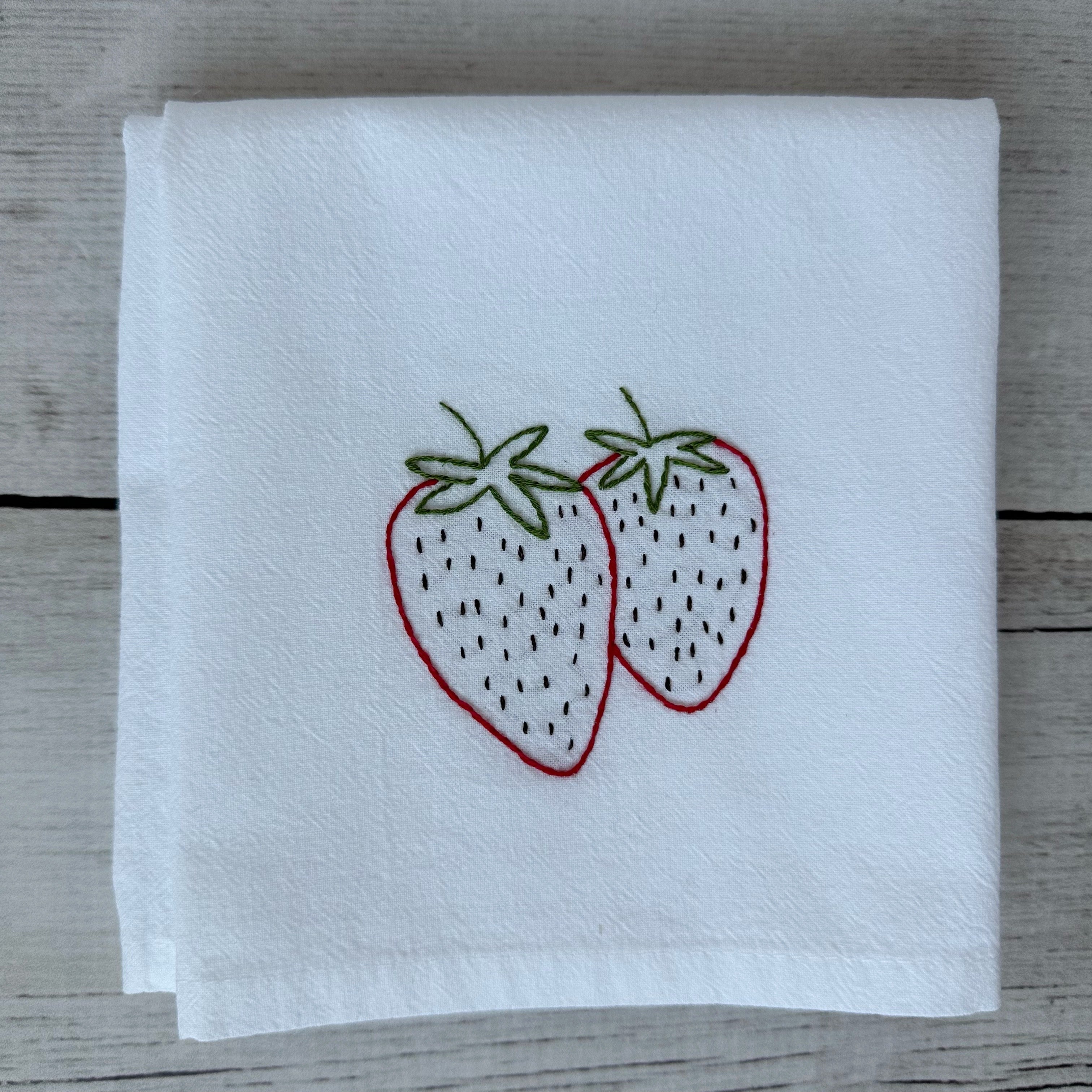 White tea towel with embroidered strawberries on a wooden surface