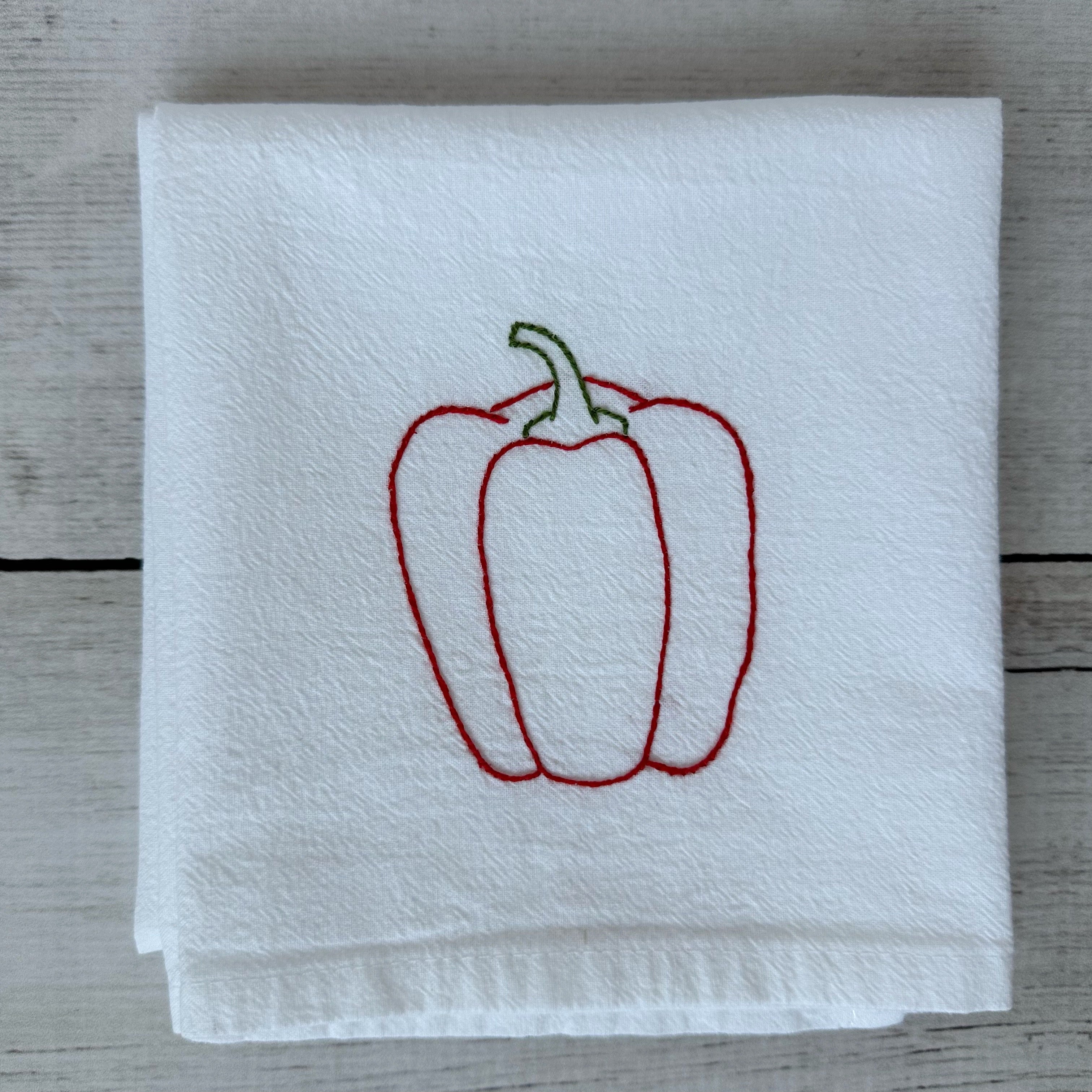 White tea towel with embroidered red bell pepper design on a wooden surface