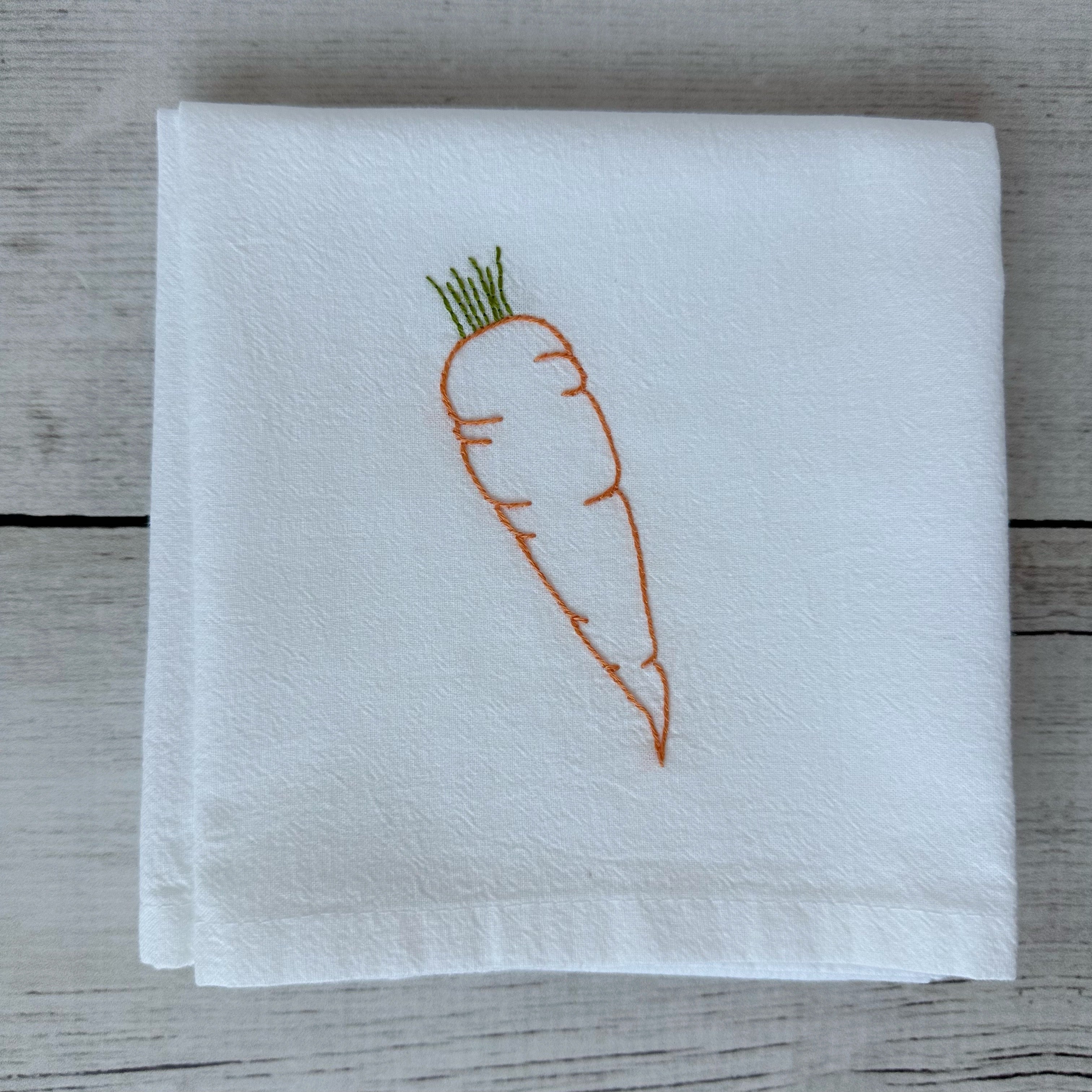 White tea towel with embroidered carrot design on a wooden surface