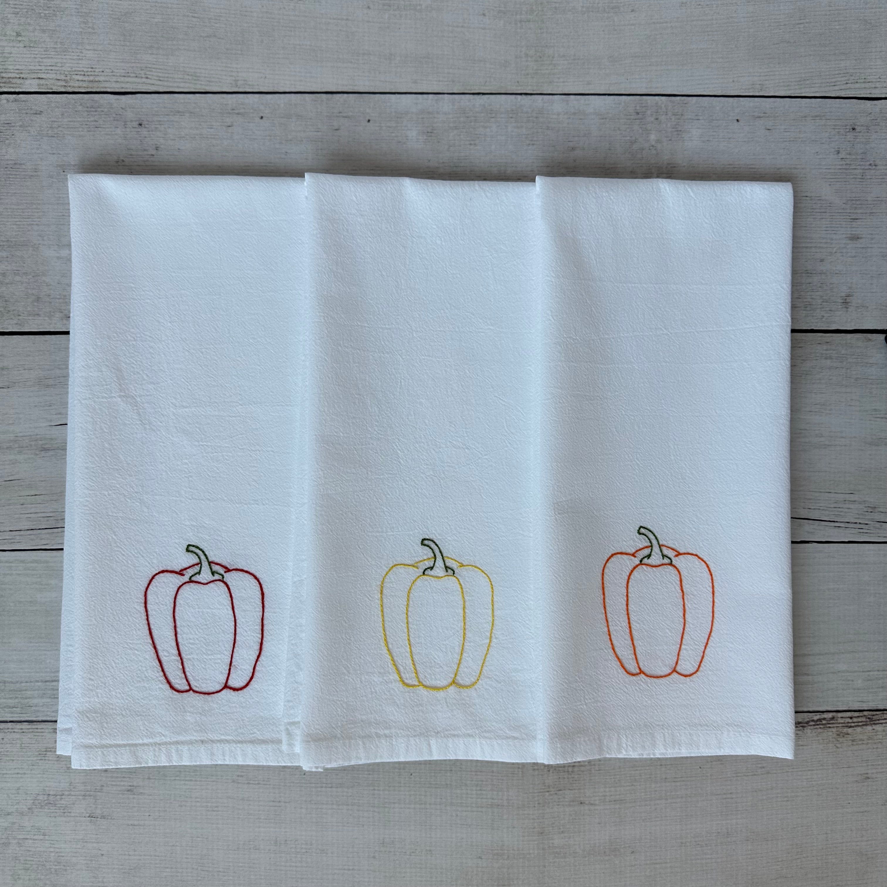 White tea towel with embroidered bell pepper designs on a wooden surface