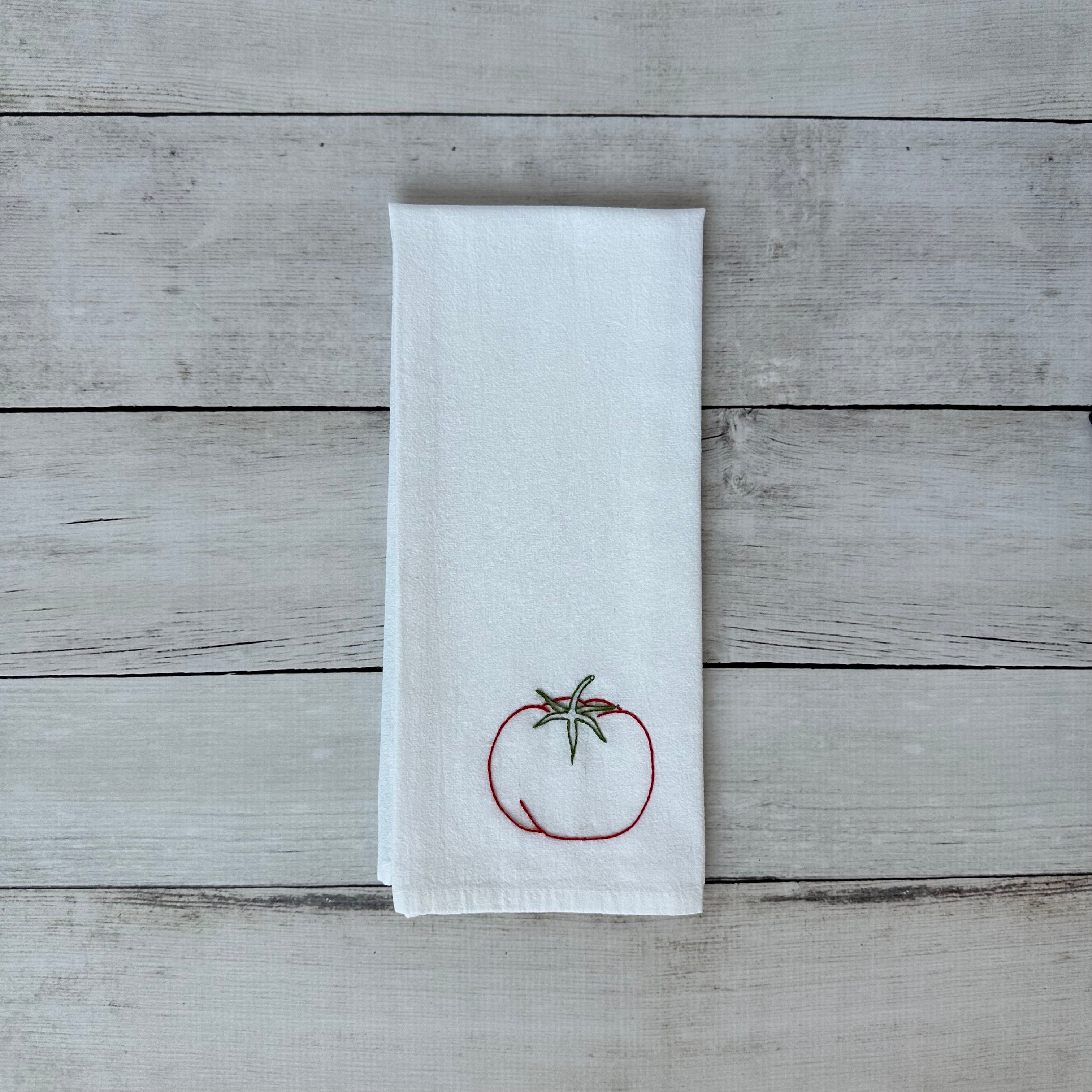 White tea towel with a tomato design on a wooden surface