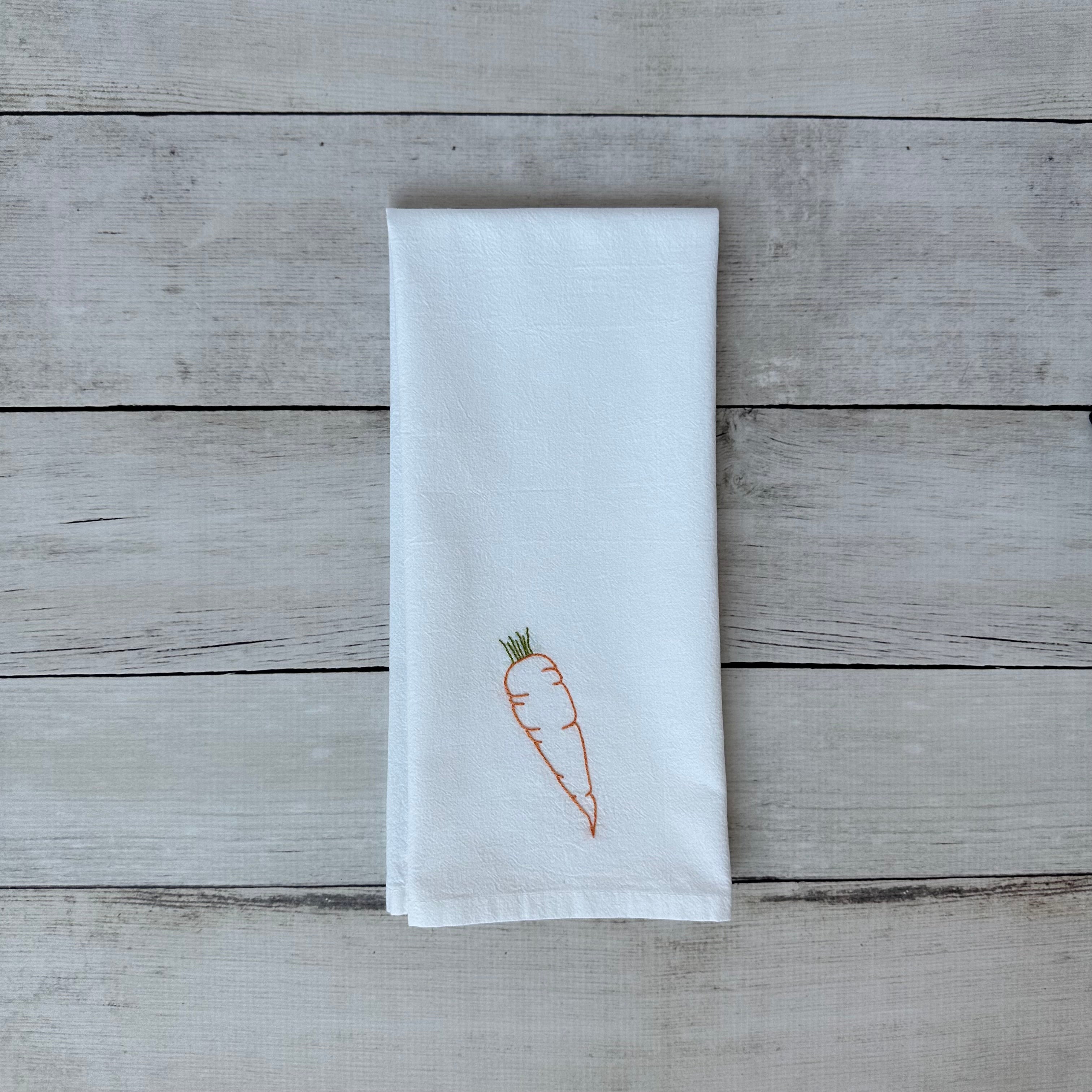 White tea towel with embroidered carrot design on a wooden surface