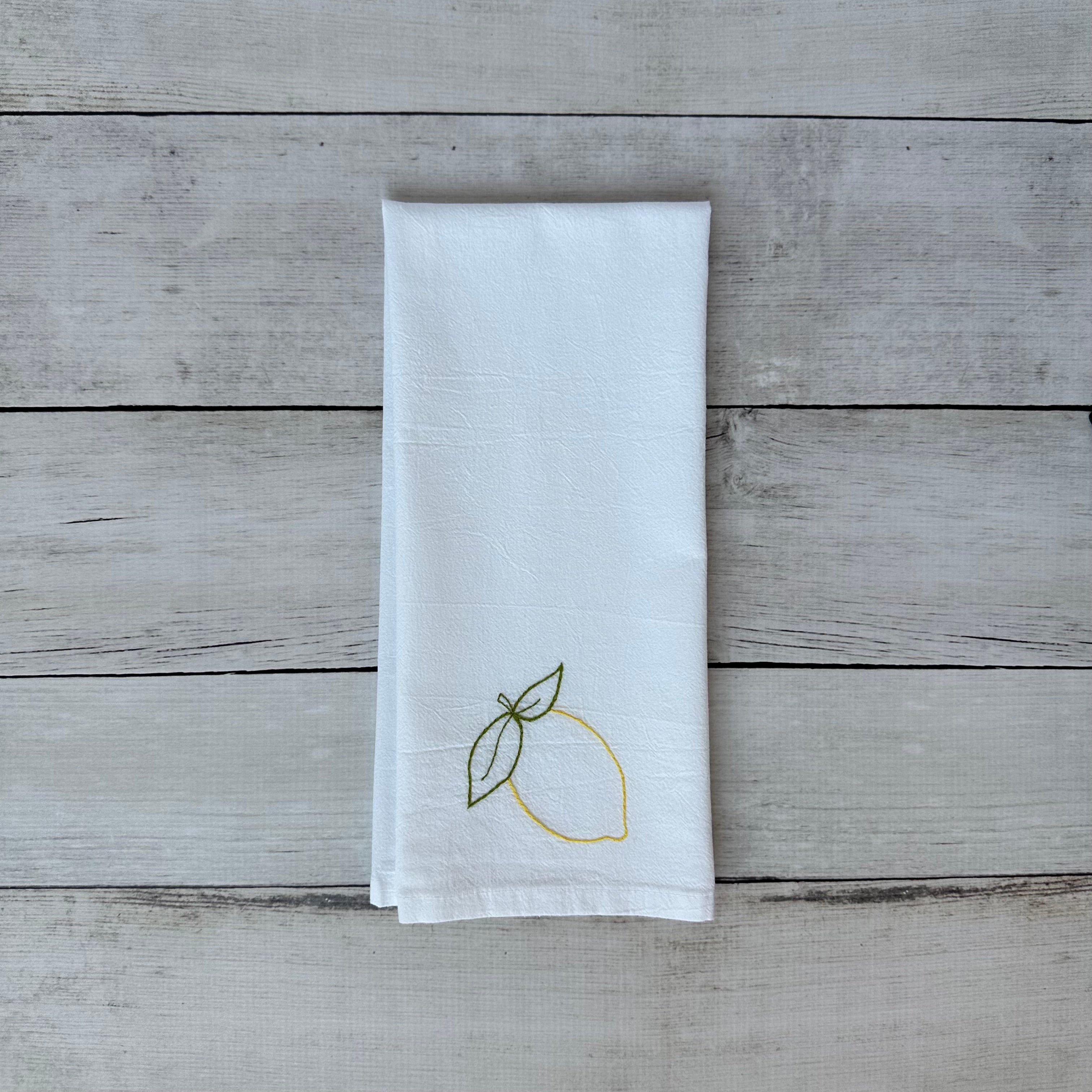 White tea towel with lemon embroidery on a wooden surface