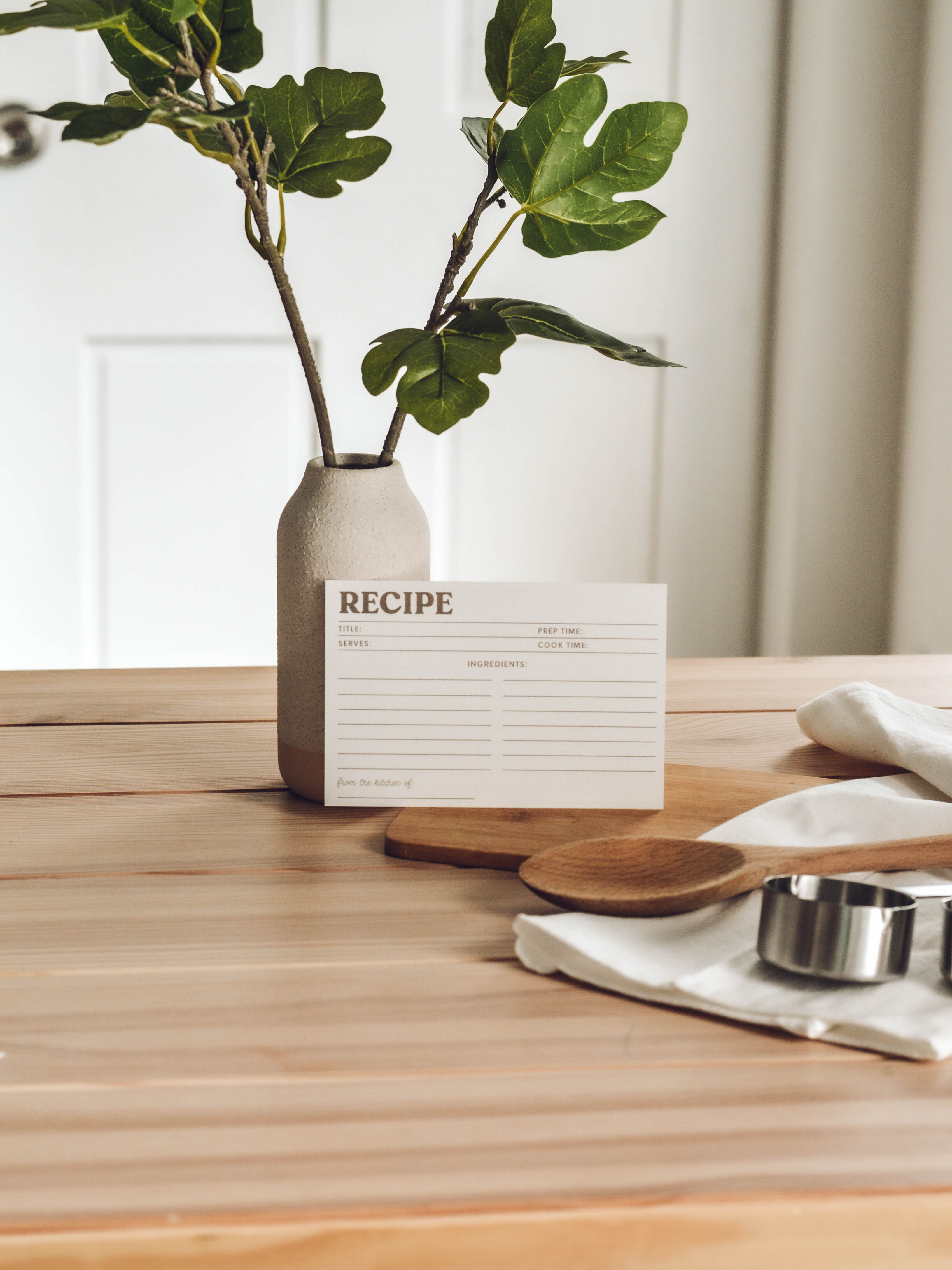 Recipe card on a wooden table with a plant and kitchen items.