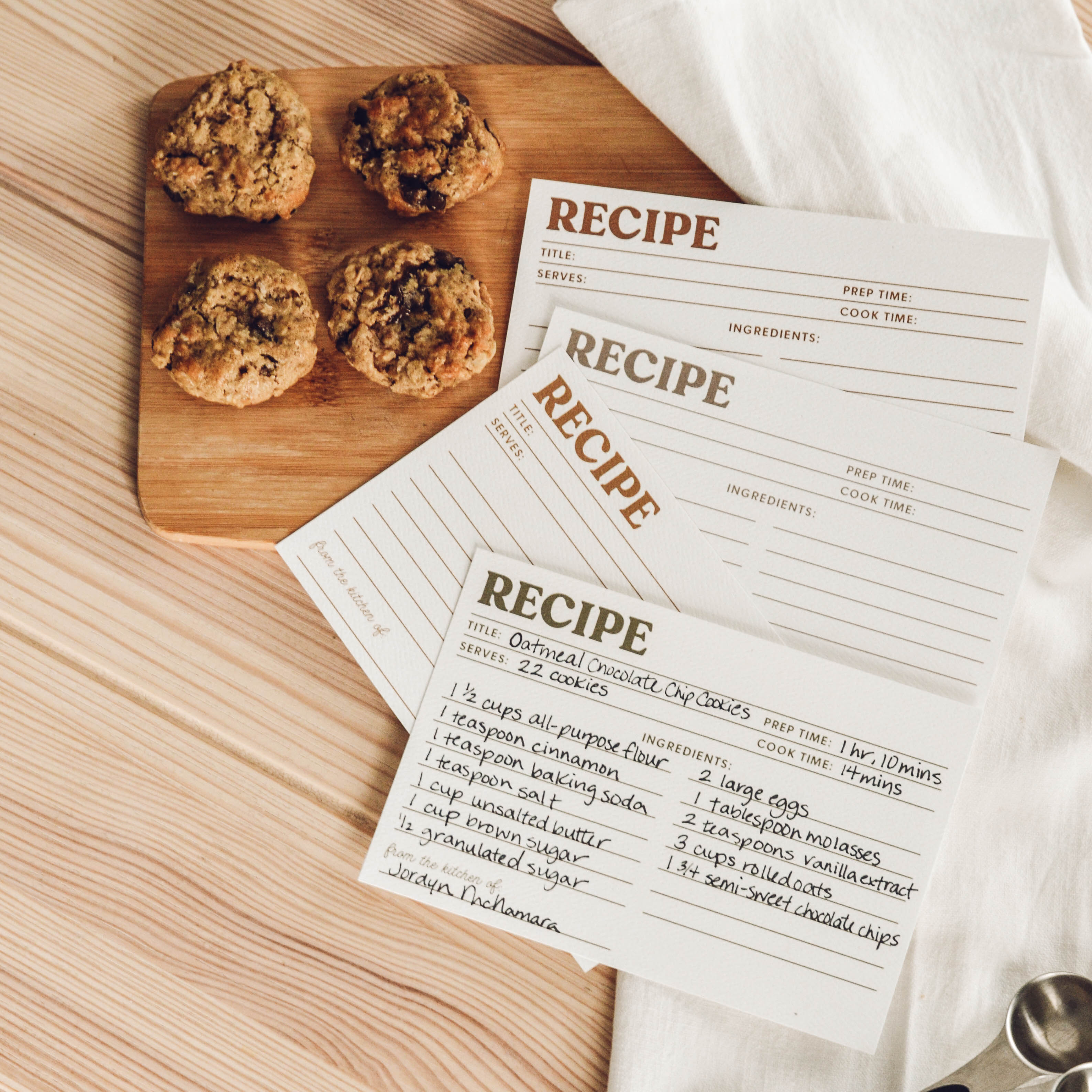 Oatmeal chocolate chip cookies on a wooden board with recipe cards on a wooden surface.