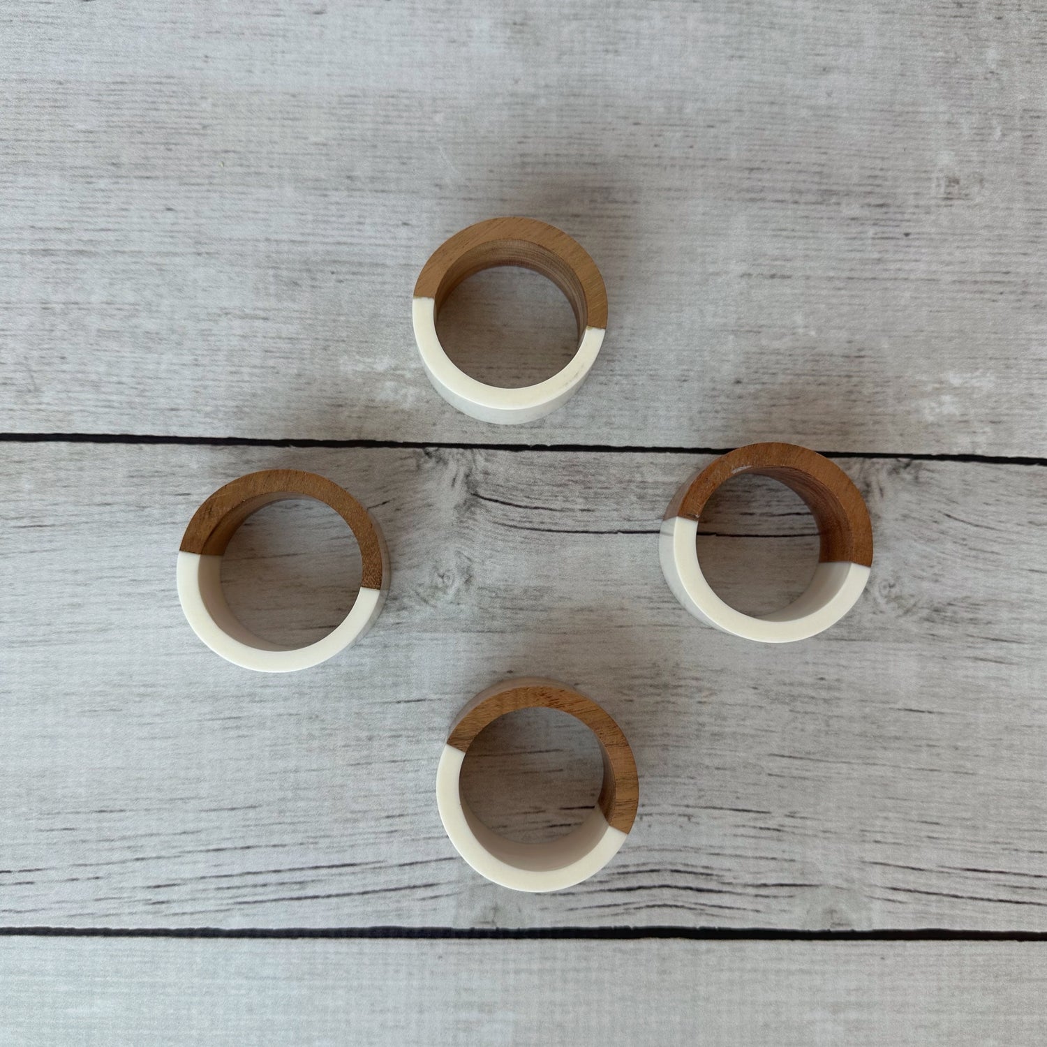 Four wooden napkin rings with white accents on a wooden surface