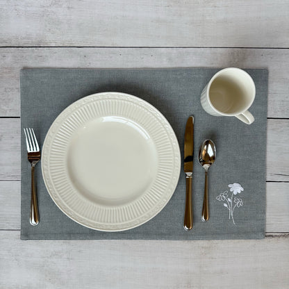 White china plate with silverware on a gray placemat with embroidered flowers on a wooden surface