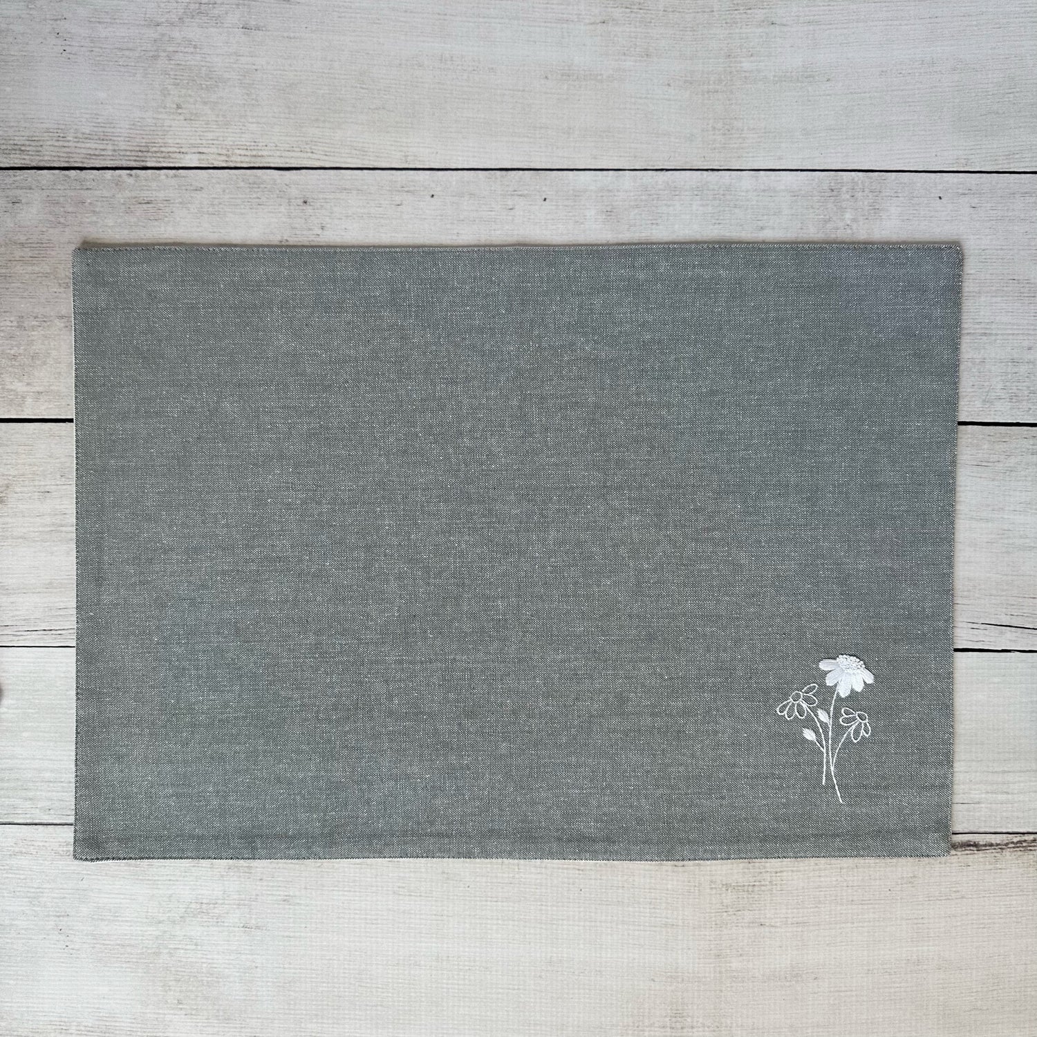 Gray cotton placemat with embroidered  floral design on a wooden surface