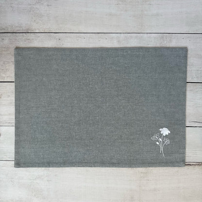 Gray cotton placemat with embroidered  floral design on a wooden surface