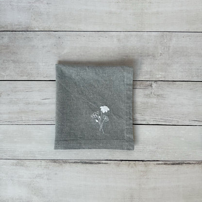 Gray cotton napkin with floral embroidered design on a wooden surface
