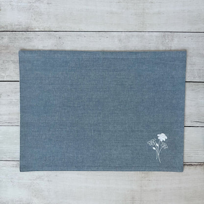 Blue cotton placemat with embroidered floral design on a wooden surface