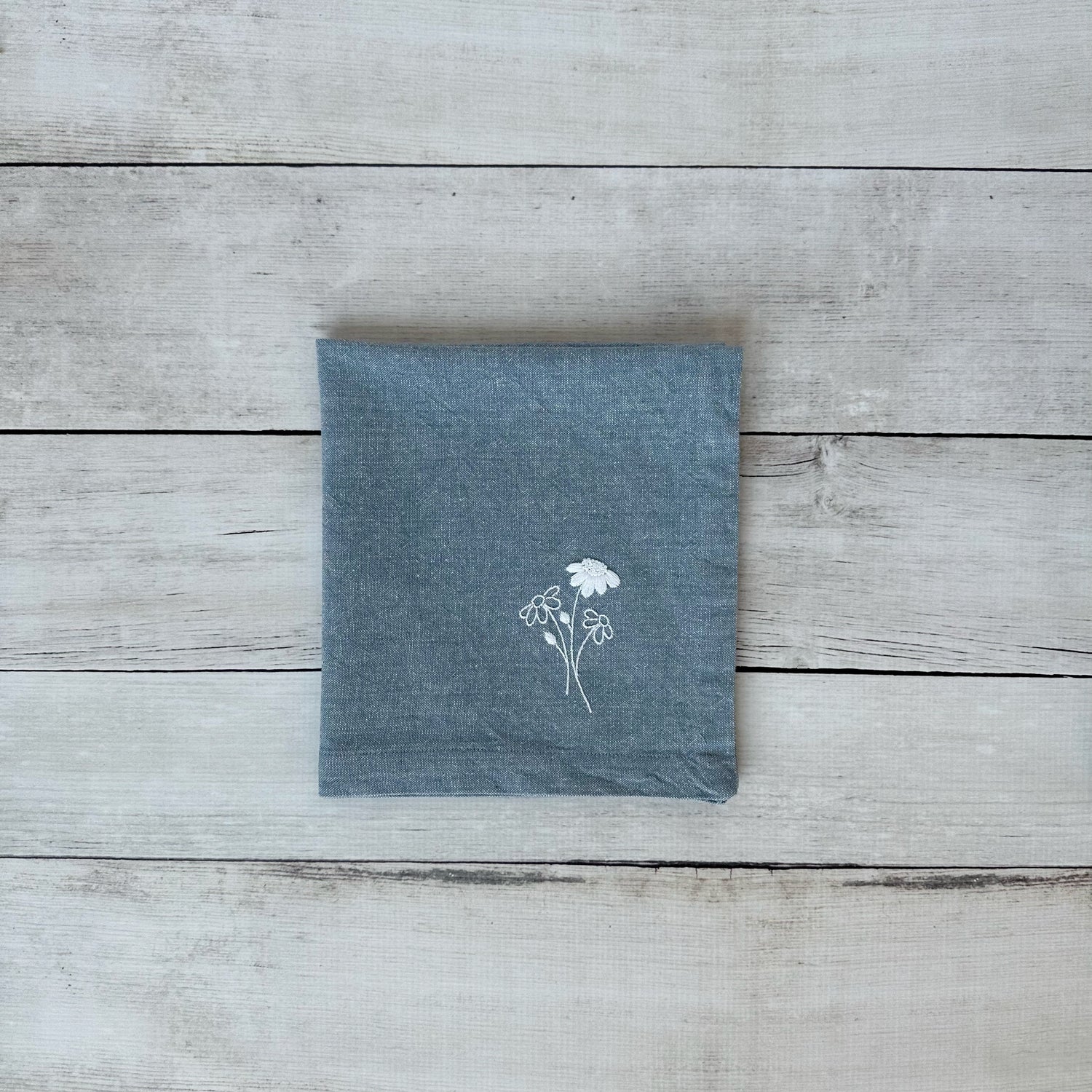 Blue cotton napkin with floral embroidered design on a wooden surface