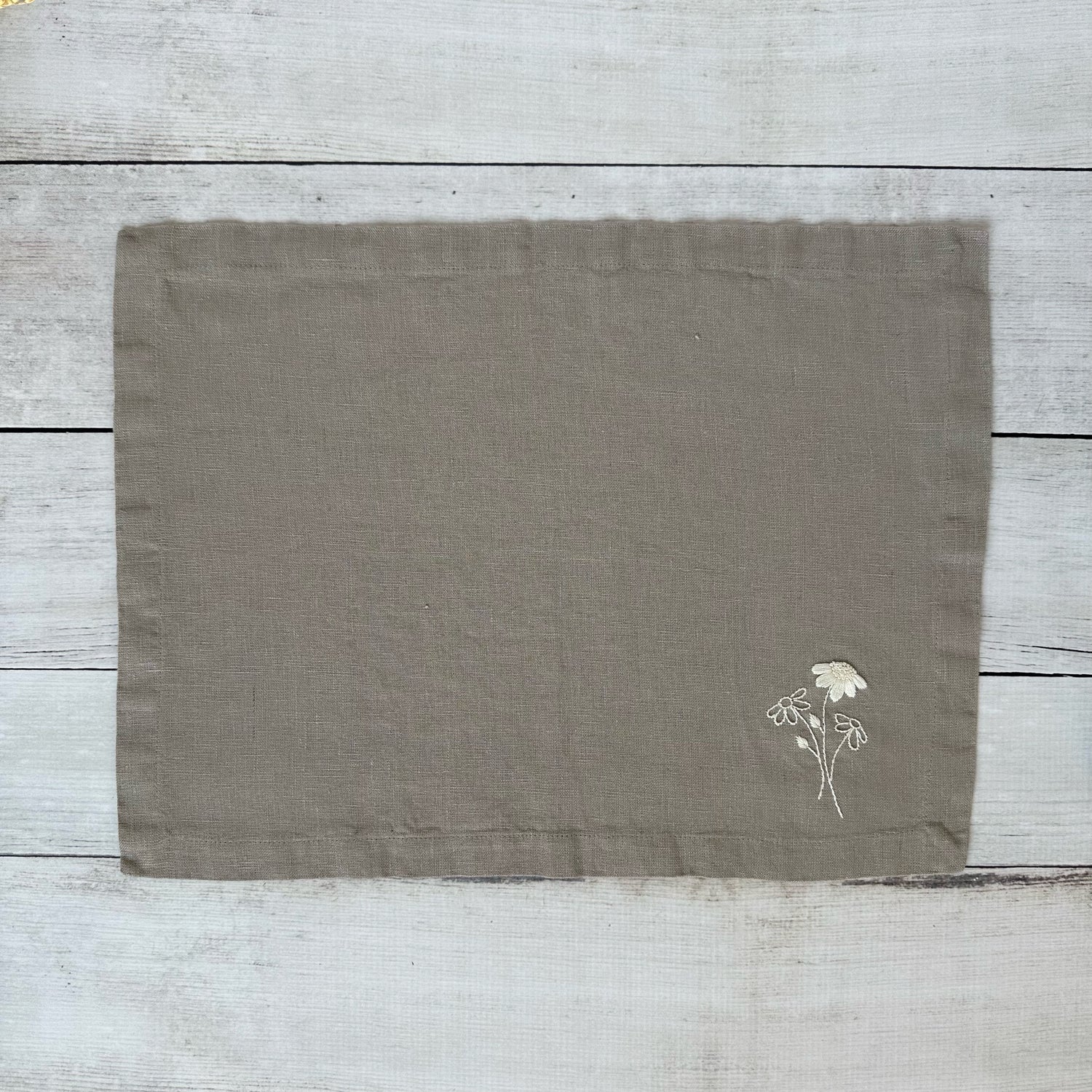 Taupe linen placemat with embroidered flowers on a wooden surface