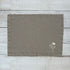 Taupe linen placemat with embroidered flowers on a wooden surface