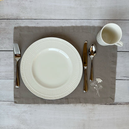 White china plate with silverware on a taupe placemat with embroidered flowers on a wooden surface
