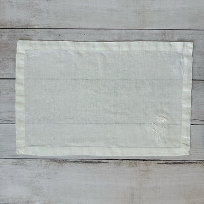 Ivory linen placemat with embroidered flowers on a wooden surface