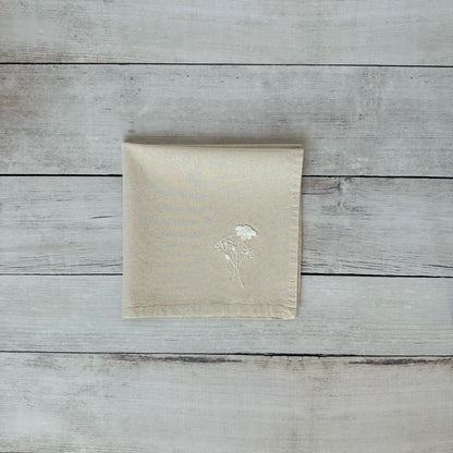 Beige napkin with embroidered floral design on a wooden surface