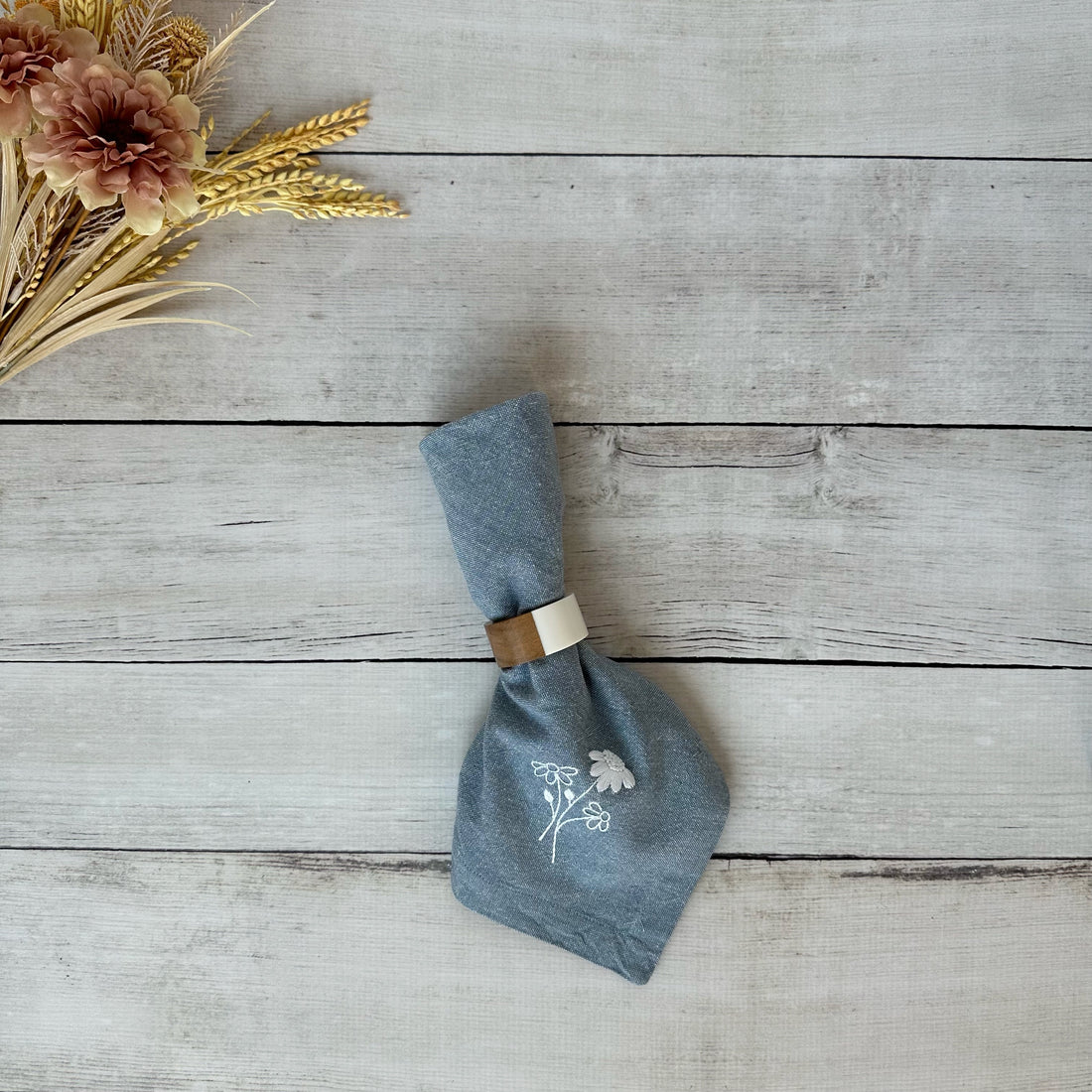 Blue cotton napkin with floral embroidery on a wooden surface with flowers.