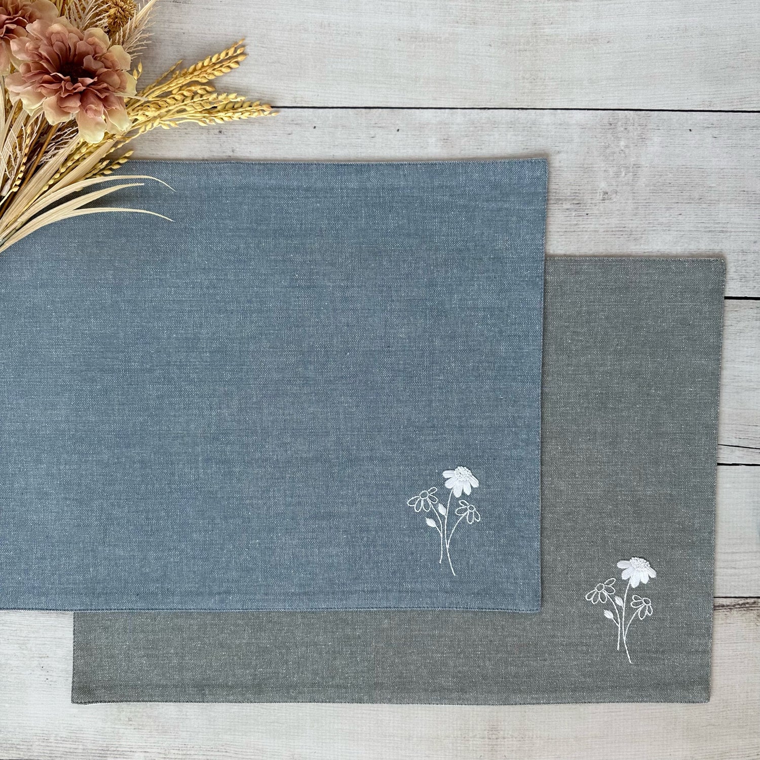 Two placemats with floral embroidery on a wooden surface.