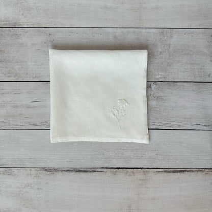 Ivory linen napkin with floral embroidered design on a wooden surface