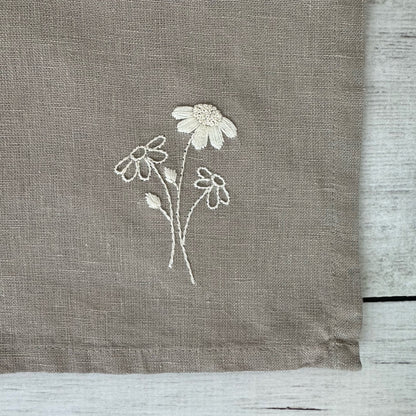 Floral embroidered design on corner of a taupe linen napkin