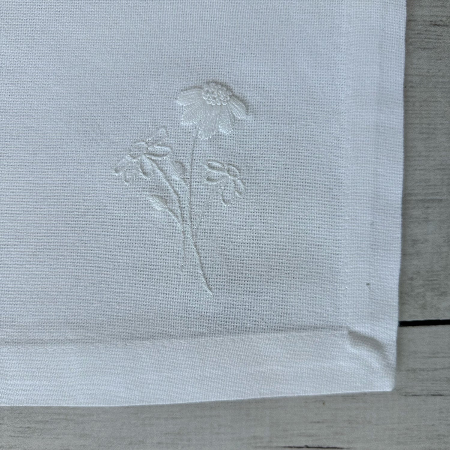 Floral embroidered design on corner of a white cotton napkin