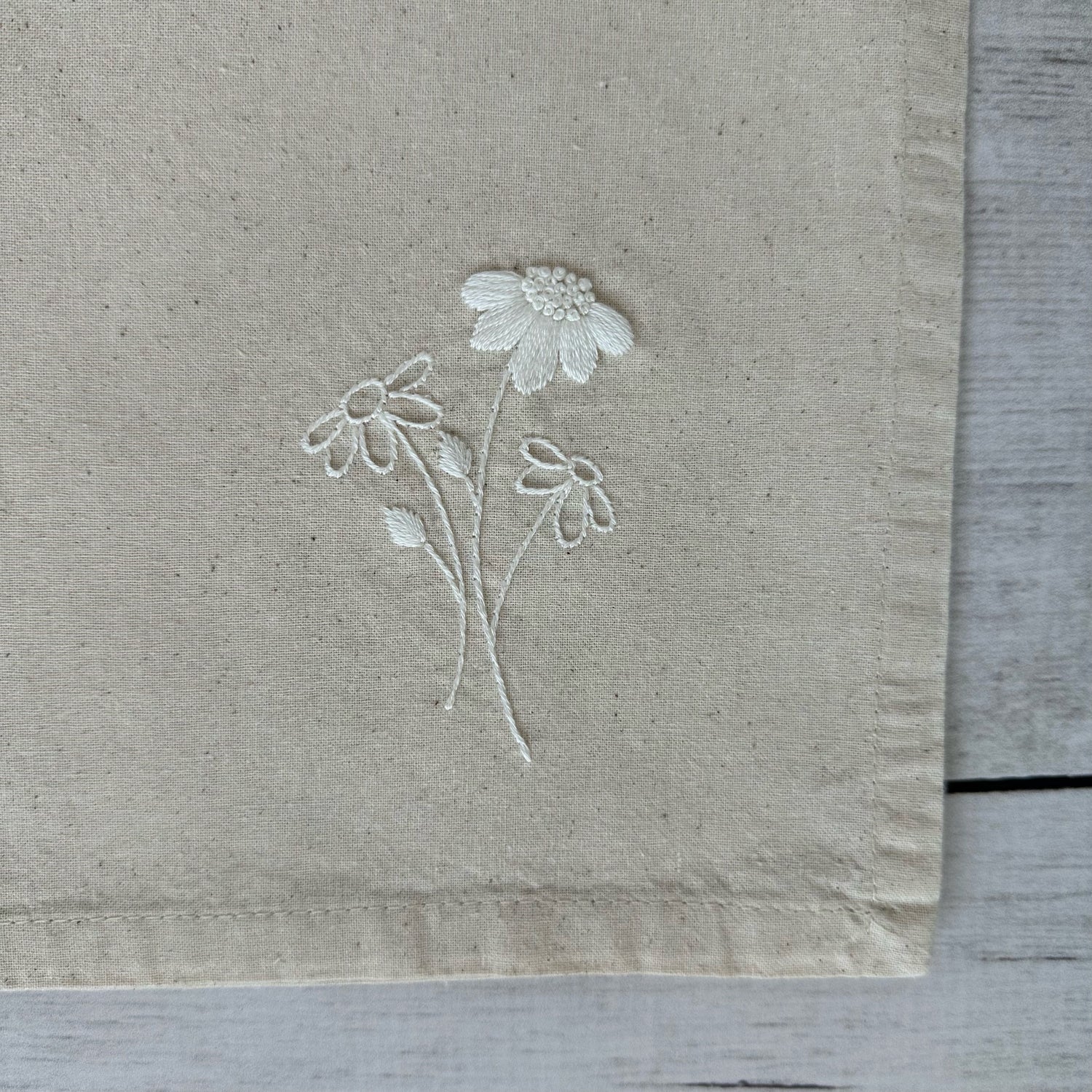 Floral embroidered design on corner of a beige cotton napkin