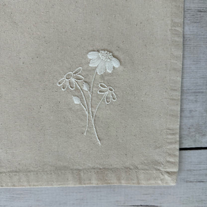 Floral embroidered design on corner of a beige cotton napkin