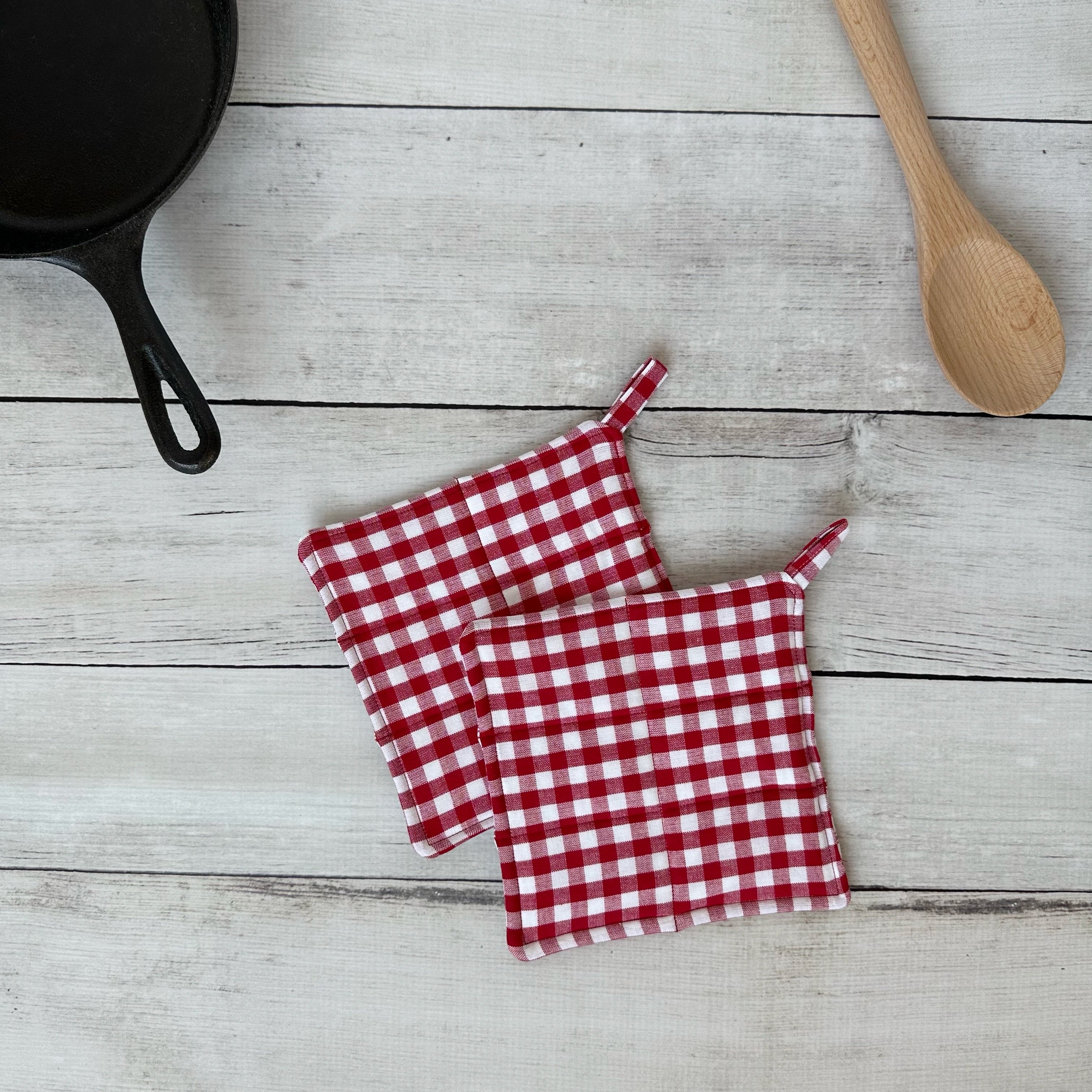 Red and white checkered pot holders on a wooden surface with a cast iron skillet and wooden spoon.